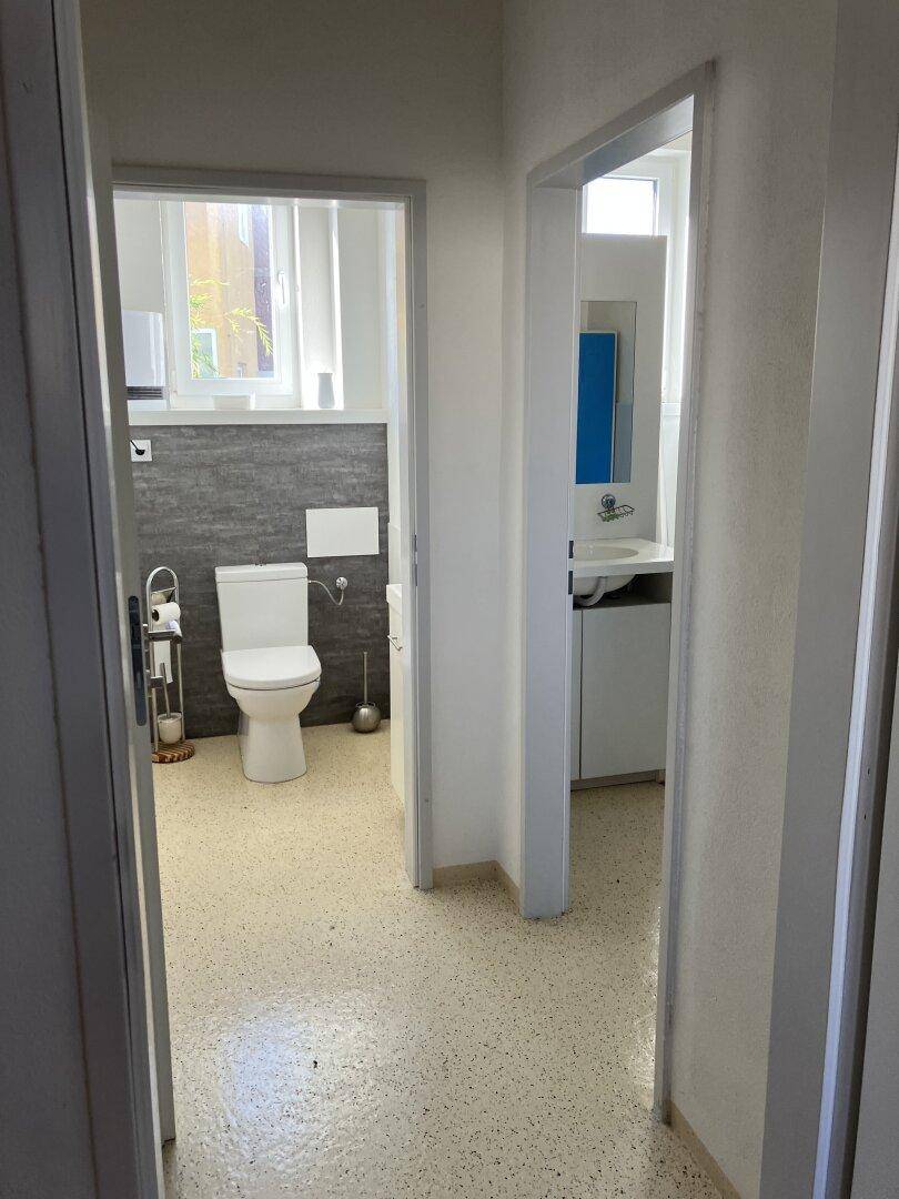Blick durch einen Flur, der zu zwei Türen führt, einem WC und einem Badezimmer.
