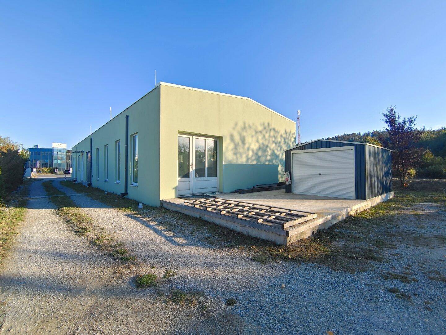 Gebäudeaußenansicht mit hellgrüner Fassade, einer kleinen Terrasse und einem Schuppen im Freien.