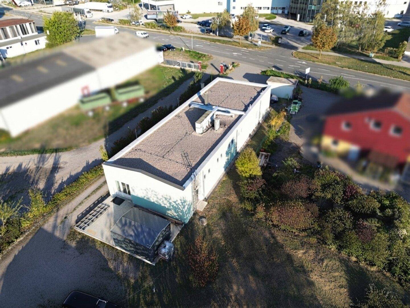 Luftaufnahme eines modernen, länglichen Gebäudes mit Flachdach und umliegendem Gelände.