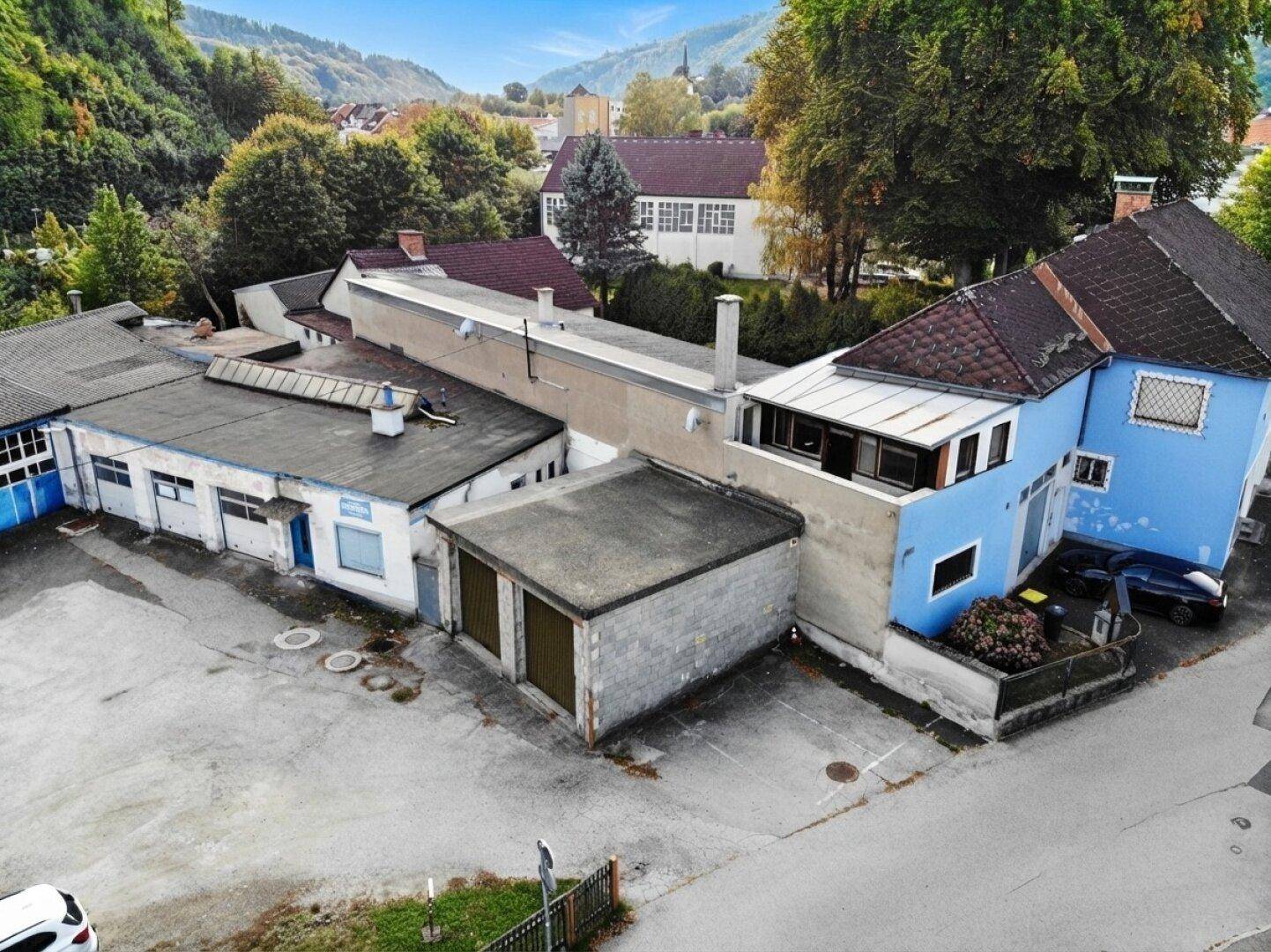 Luftaufnahme des blauen Gebäudes mit einem langen Anbau und weiteren Industriegebäuden.