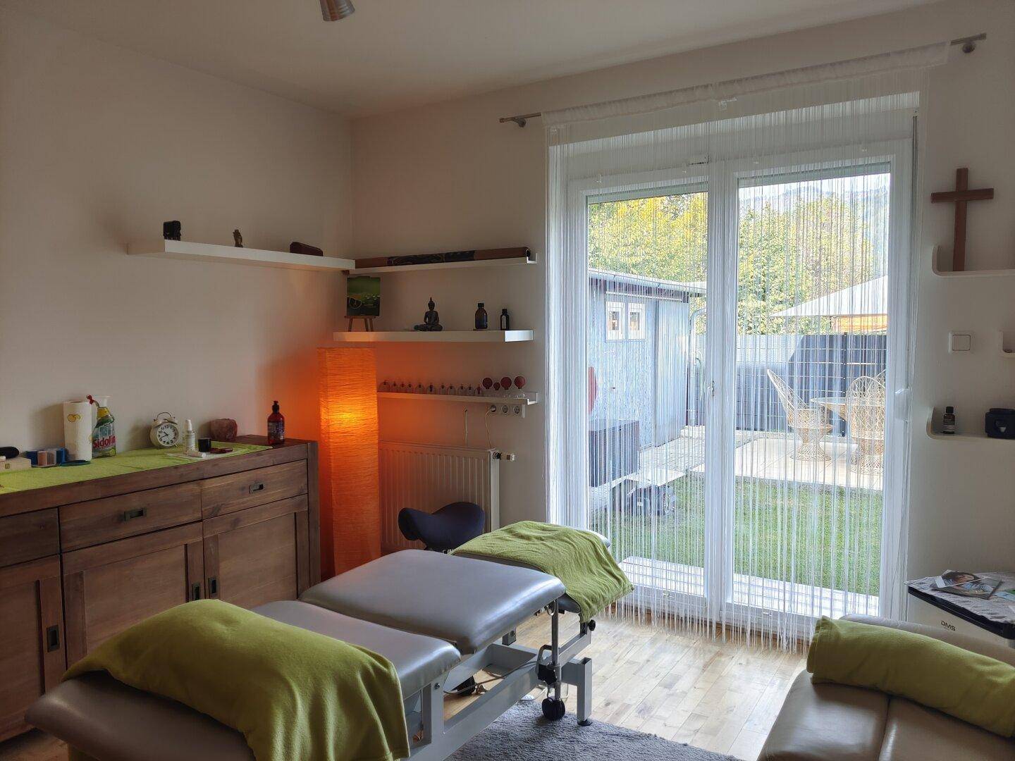 Helles Zimmer mit Holzboden, Gartenzugang und einer Liege, ideal als Büro oder Therapieraum nutzbar.