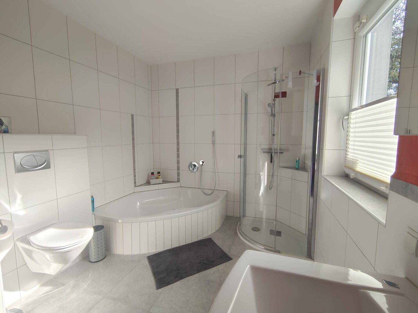 Modernes Badezimmer mit Eckbadewanne, Duschkabine, WC und Fenster für angenehmes Tageslicht.