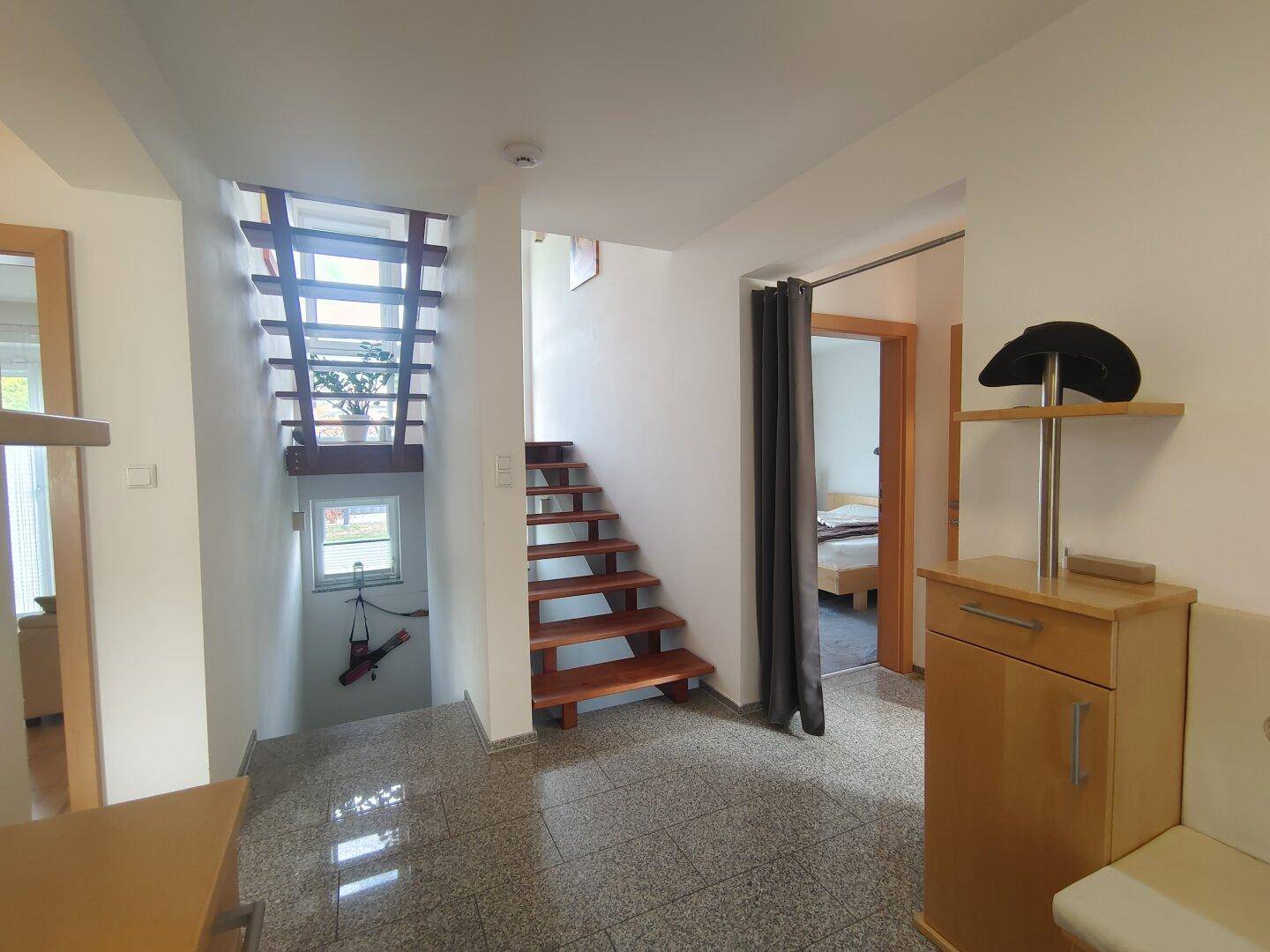 Geräumiger Flur mit offener Holztreppe, Fliesenboden und Zugang zu weiteren Räumen im Haus.