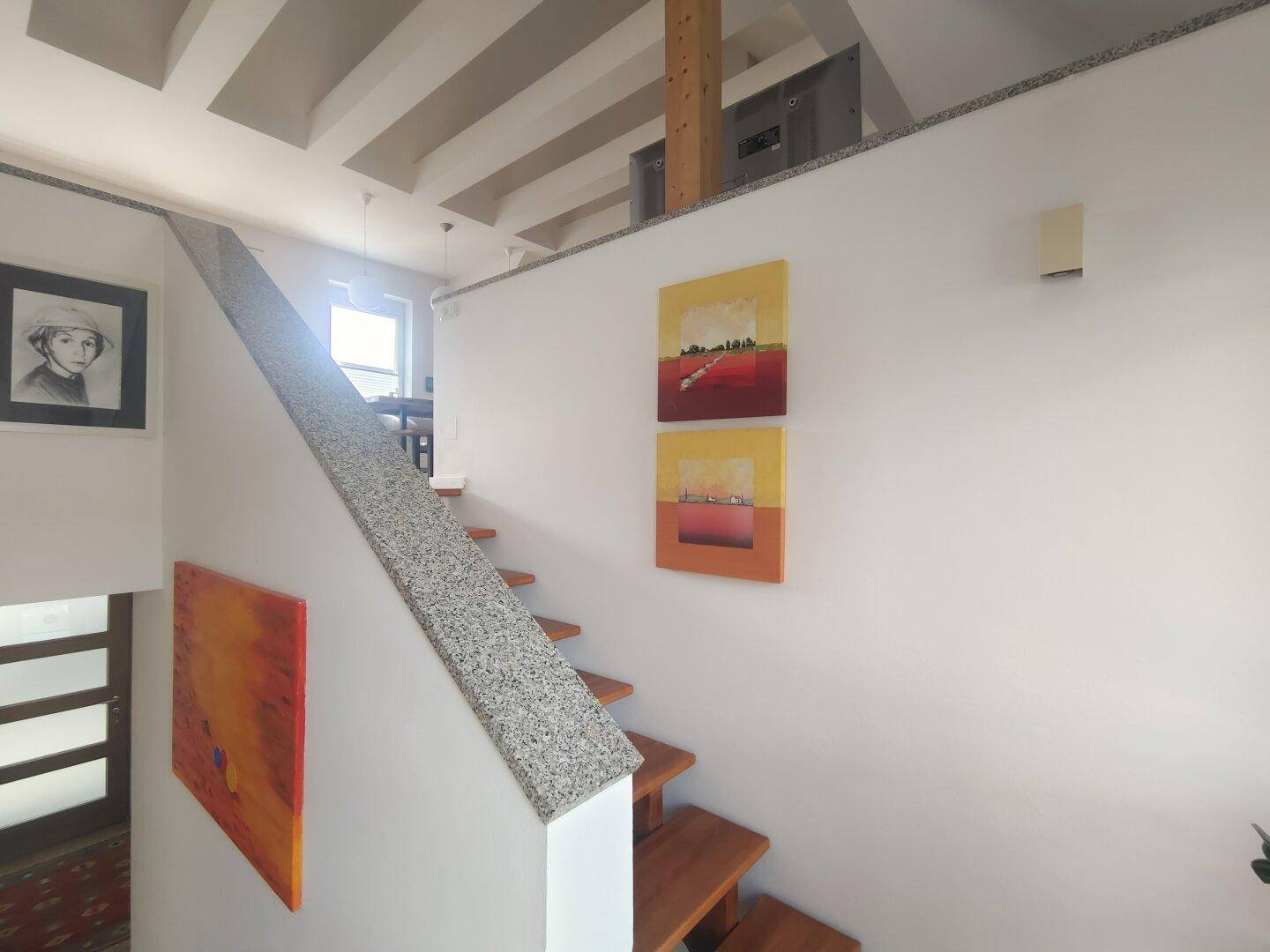Offener Treppenbereich mit Holzstufen, Granitgeländer und moderner Kunst an den Wänden des Flurs.
