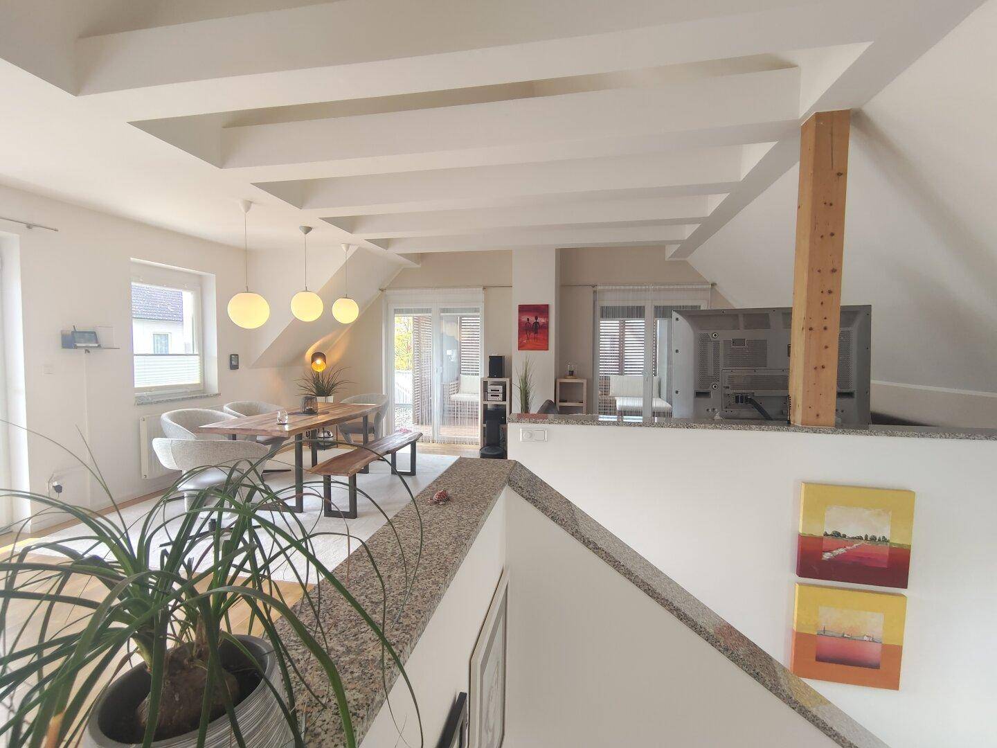 Großzügiger, offener Wohn-Essbereich mit Holzbalkendecke, Parkettboden und Zugang zum Balkon.