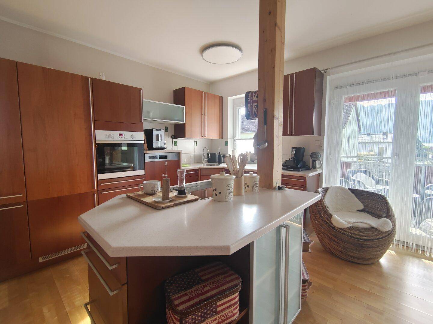 Moderne Einbauküche mit Holzfronten, Kücheninsel und direktem Zugang zum sonnigen Balkon.