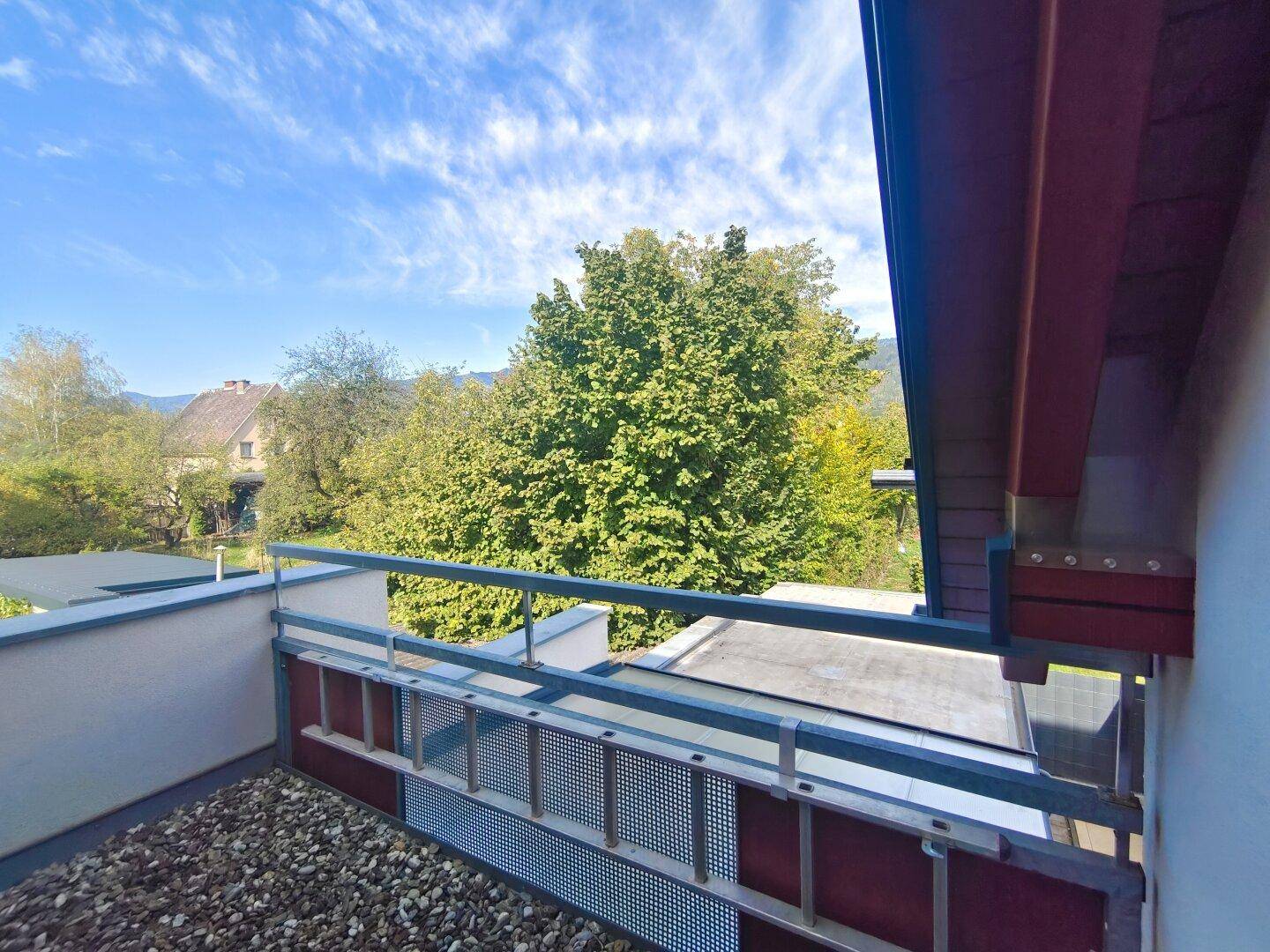 Kleiner Balkon mit Kiesboden und weitem Blick auf grüne Bäume und die umliegende Landschaft.