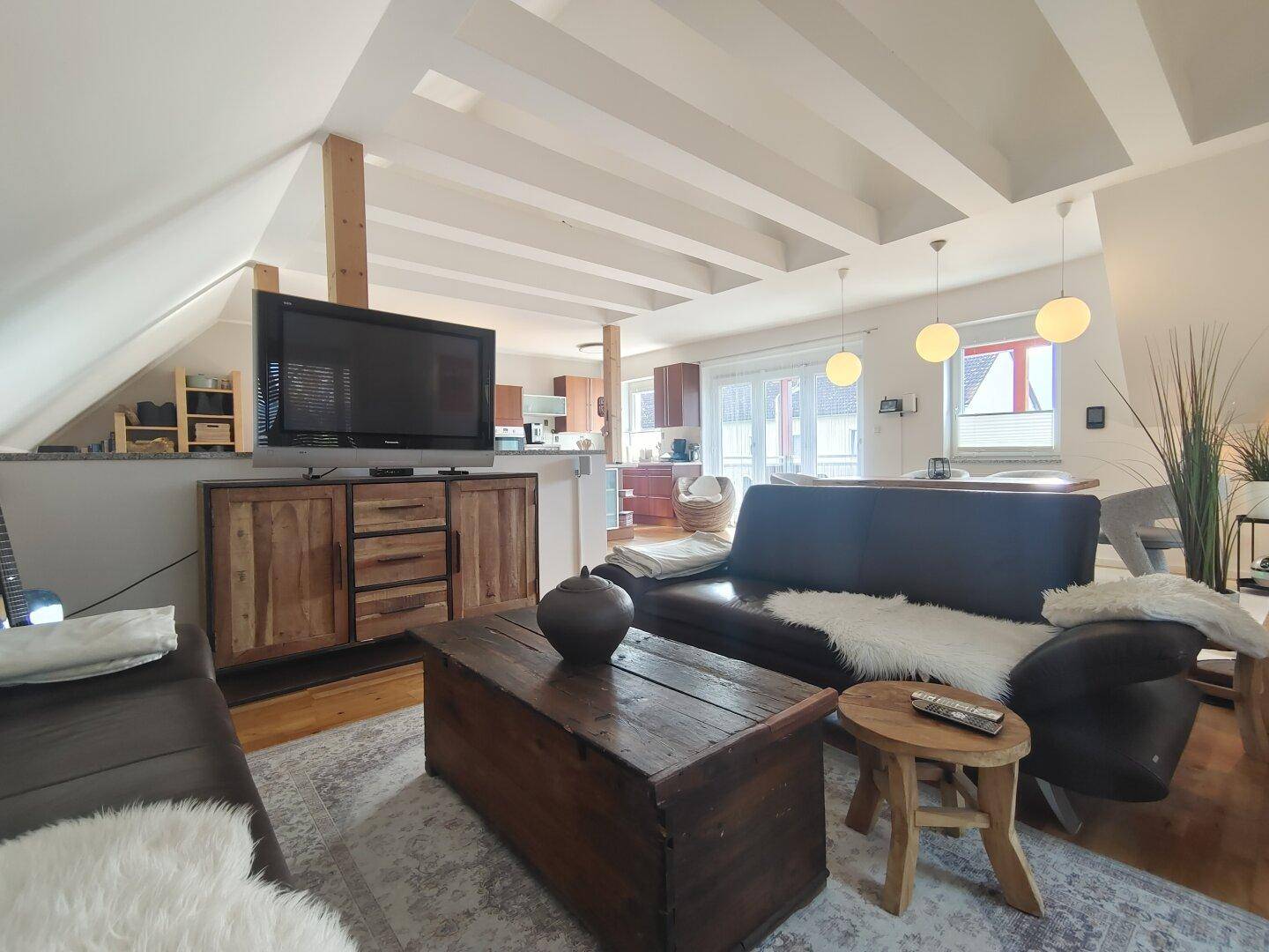 Gemütlicher Wohnbereich mit Ledersofa, Holztisch und Blick auf den offenen Küchenbereich.