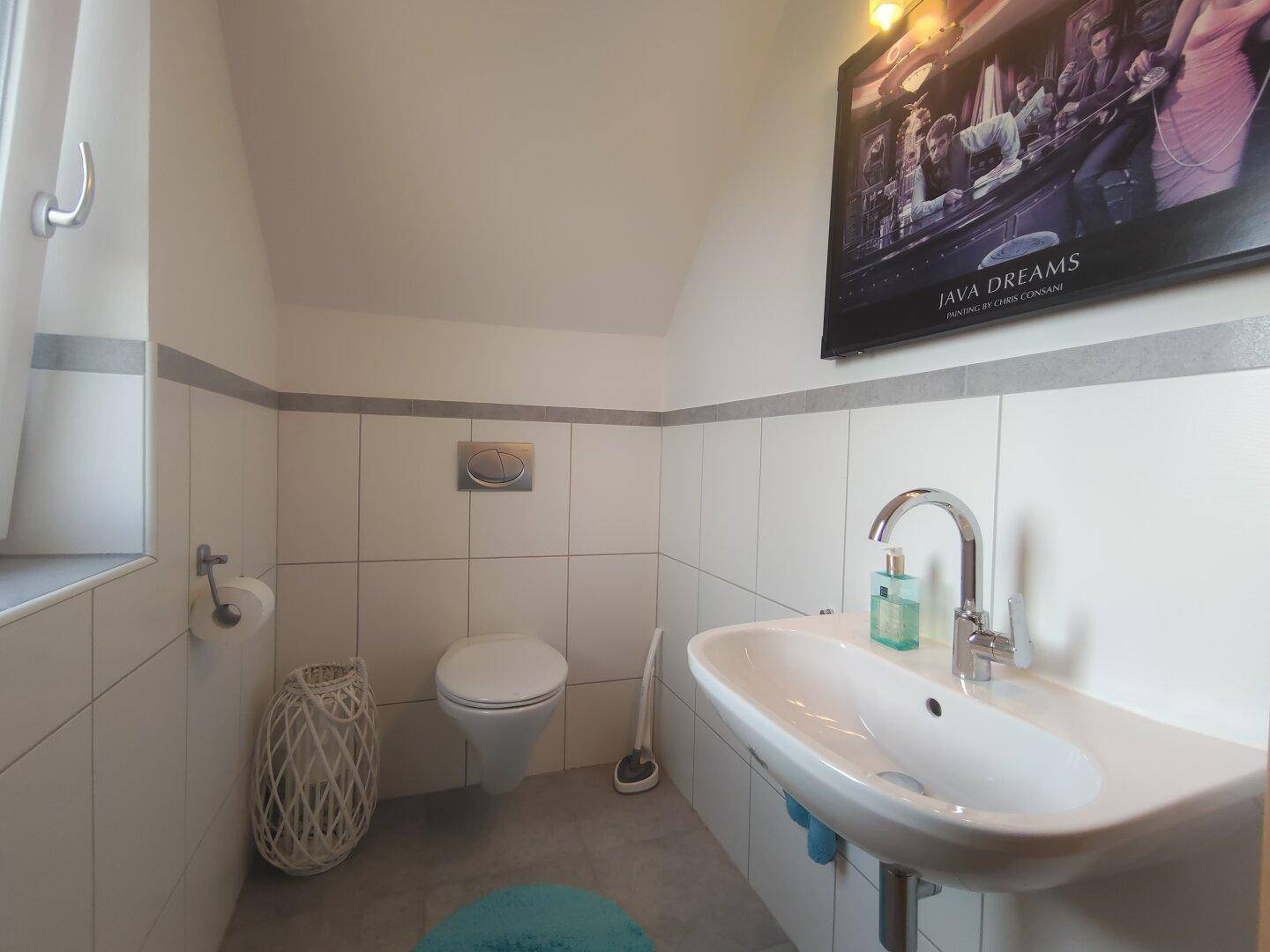 Modernes Gäste-WC mit wandhängendem WC, Waschbecken und Fenster für natürliche Belüftung.
