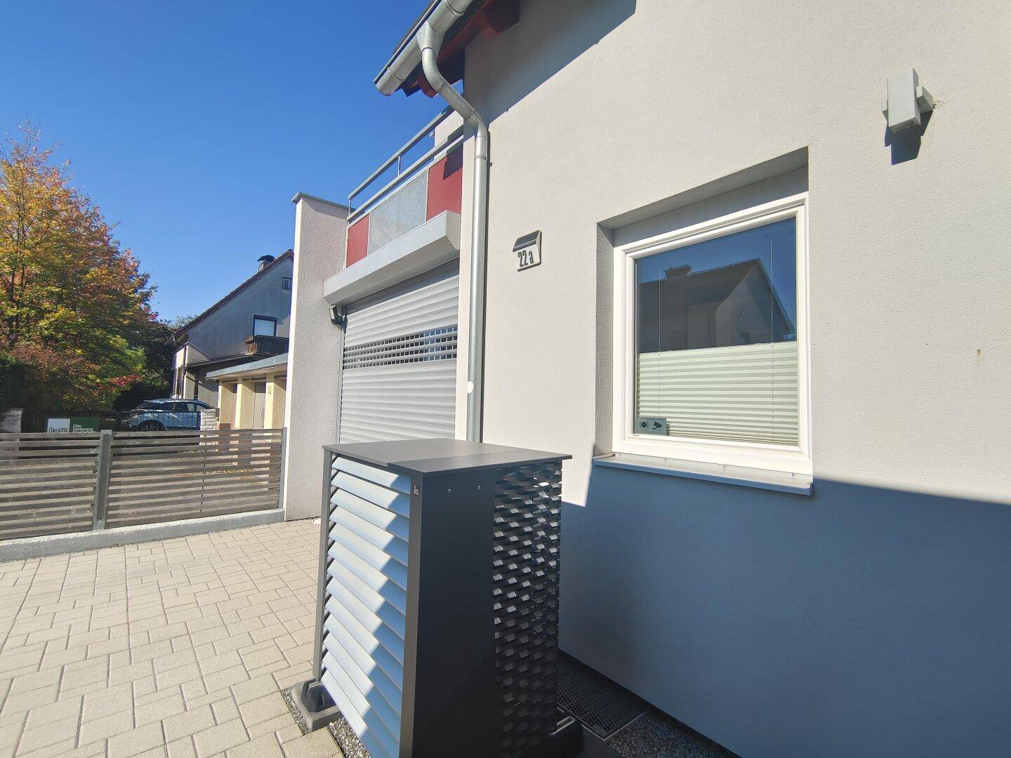Hausfassade mit gepflasterter Einfahrt und einer modernen Außeneinheit für die Wärmepumpe.