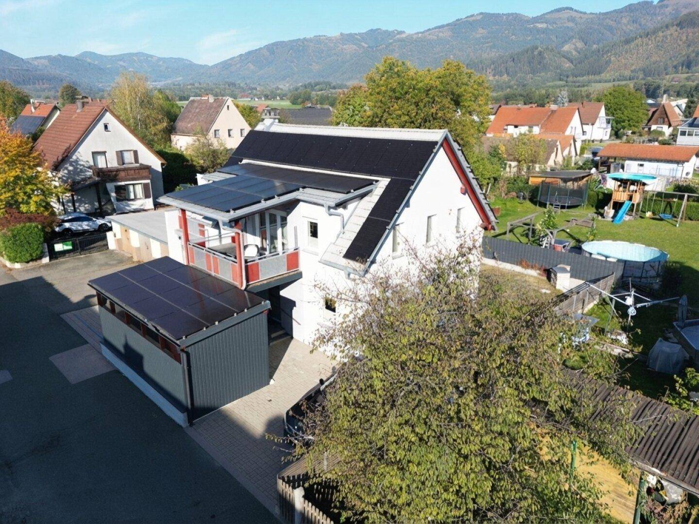 Weitläufige Luftaufnahme des Hauses mit Photovoltaikanlage, Garten und Bergblick im Hintergrund der Landschaft.