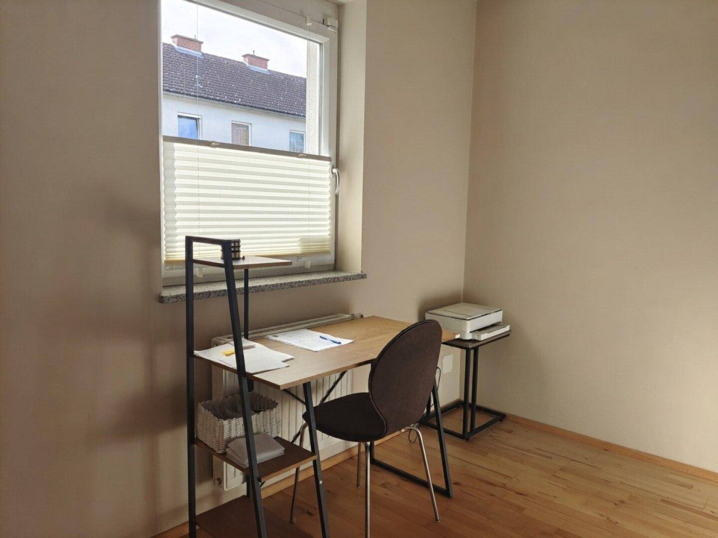 Kleines, helles Büro mit Holzboden, Schreibtisch und Fensterblick auf die umliegenden Gebäude.