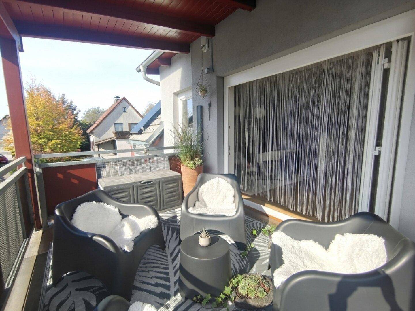 Gemütlicher Balkon mit modernen Sitzgelegenheiten, Teppich und Blick auf die grüne Umgebung.