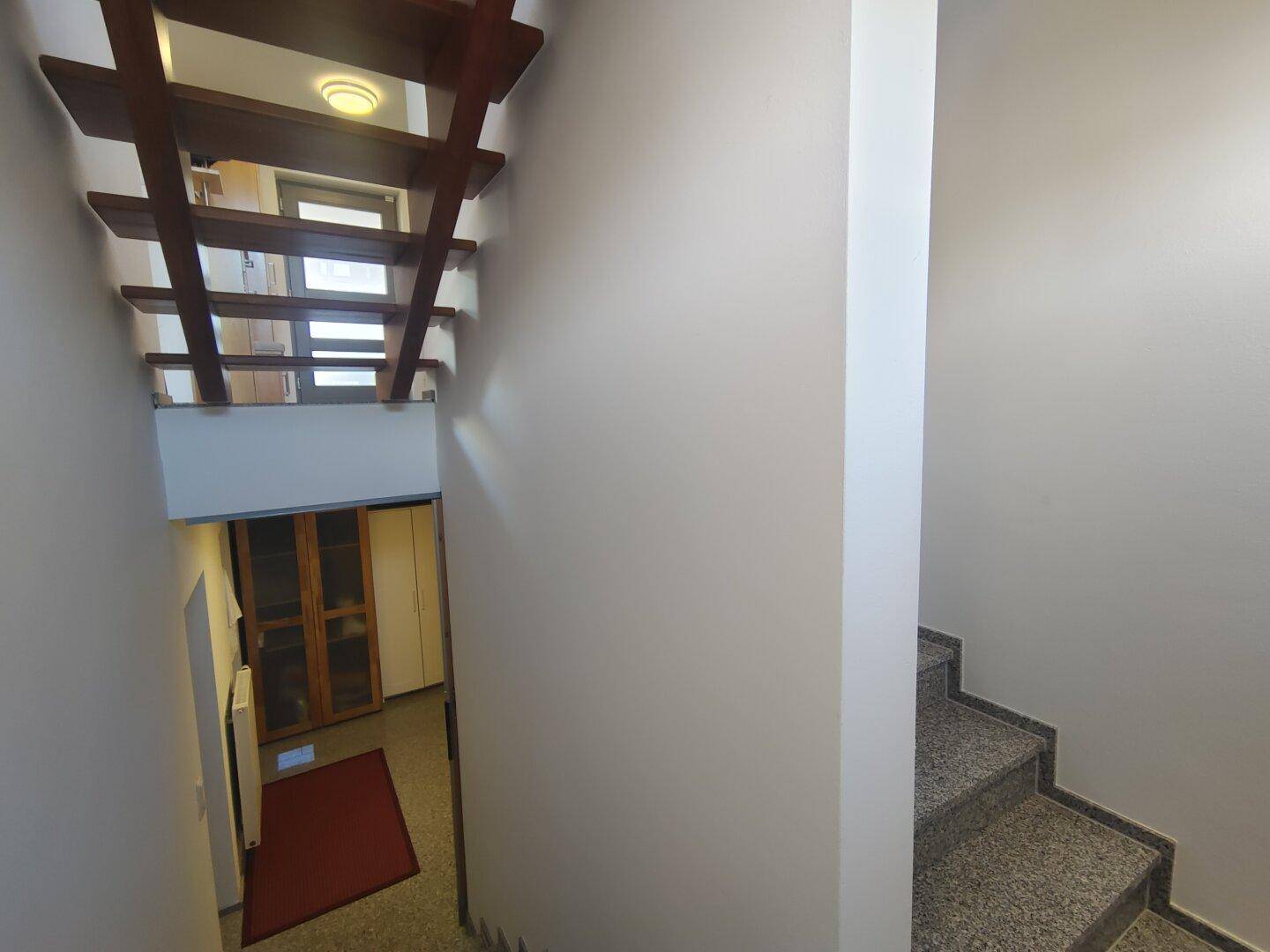 Treppenhaus mit Holzstufen und Fliesenboden, das verschiedene Ebenen des Hauses miteinander verbindet.