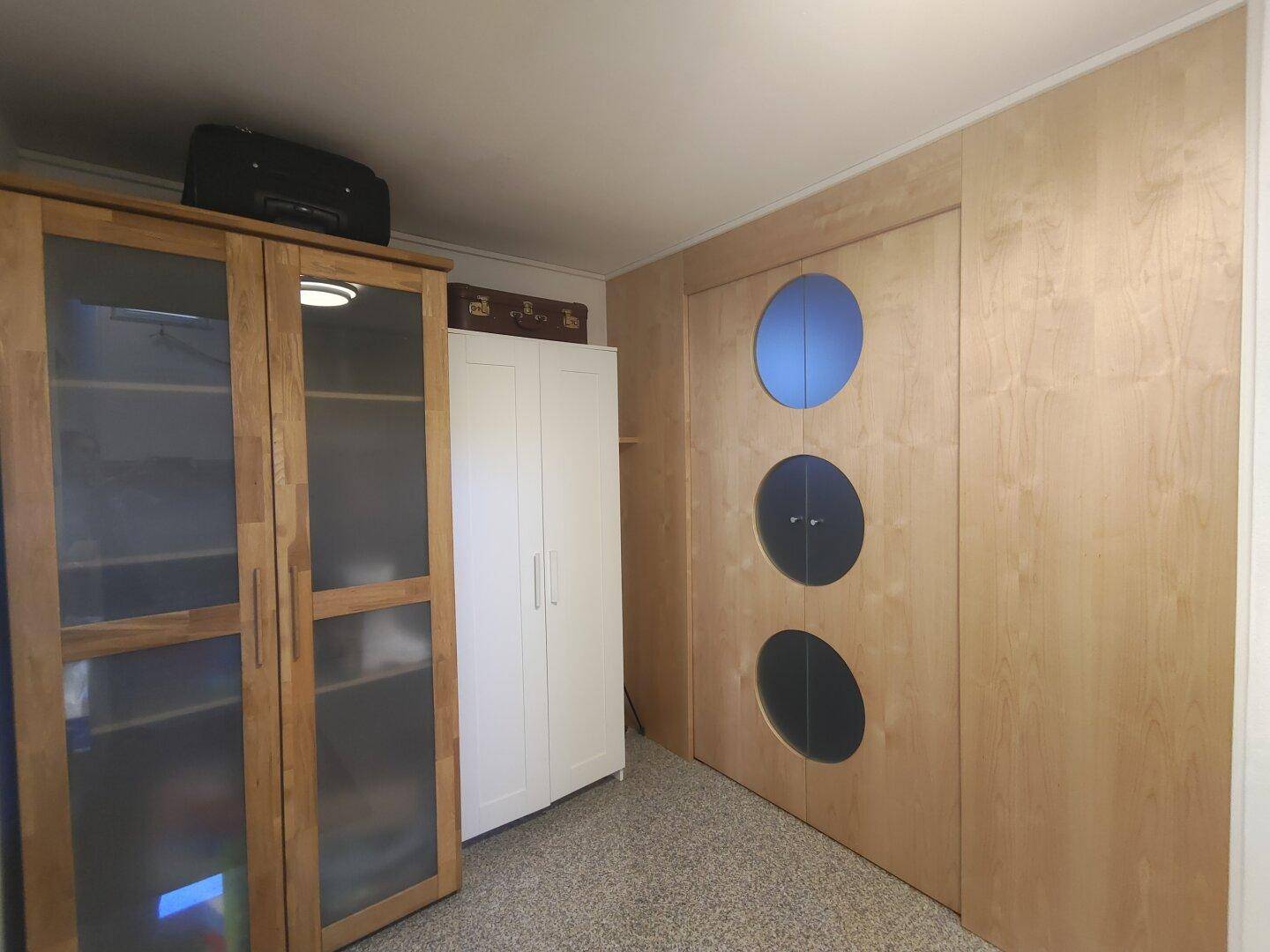 Zimmer mit maßgefertigten Holzschränken, Teppichboden und dekorativen runden Fenstern in der Wand.