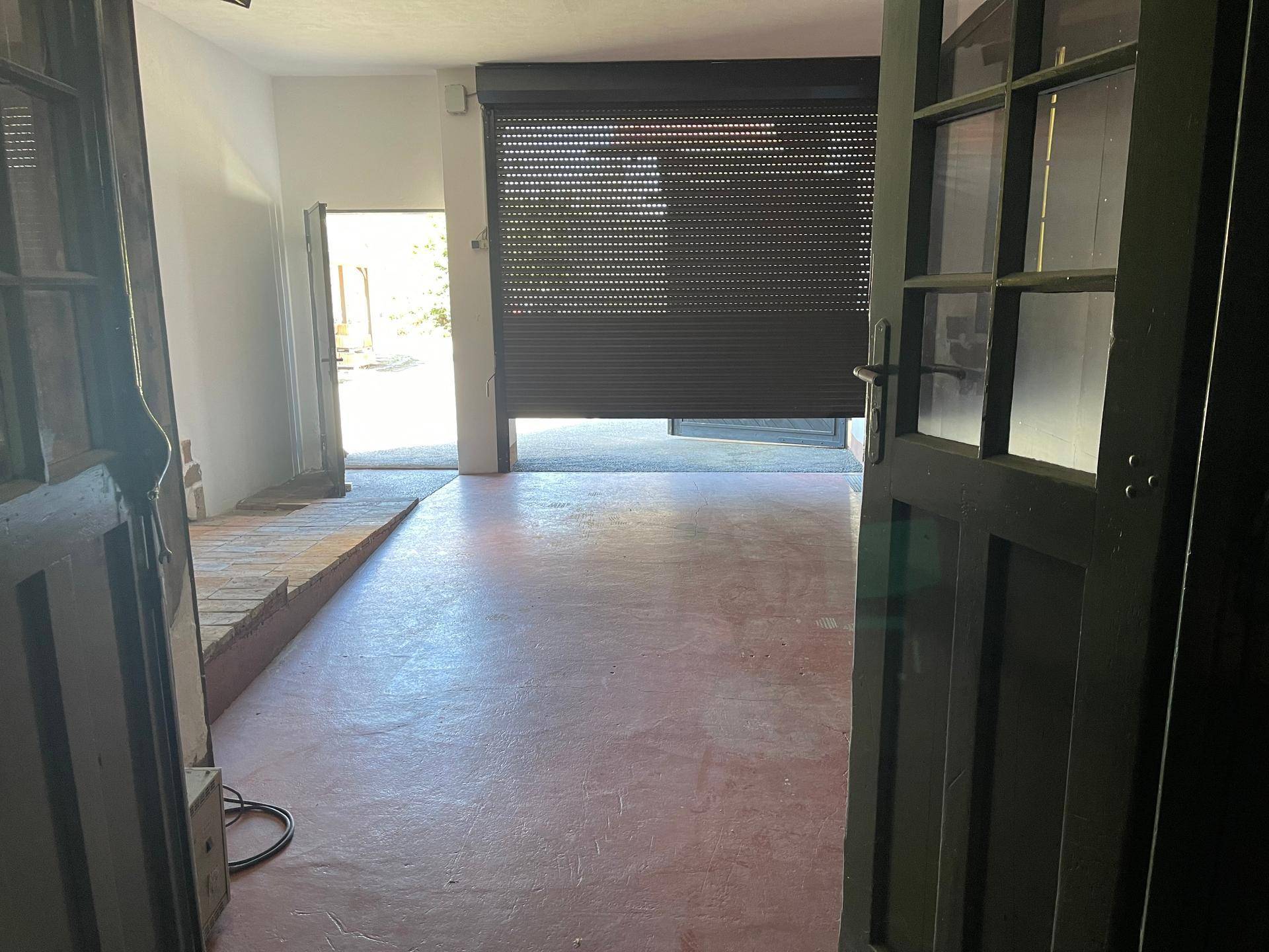 Innenraum mit rotem Boden und einer geschlossenen Rolltür, die zu einem Außenbereich führt.