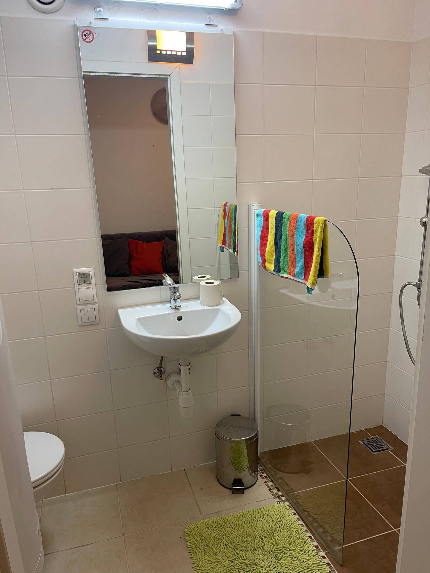 Badezimmer mit weißen Fliesen, Duschkabine und kleinem Waschbecken.