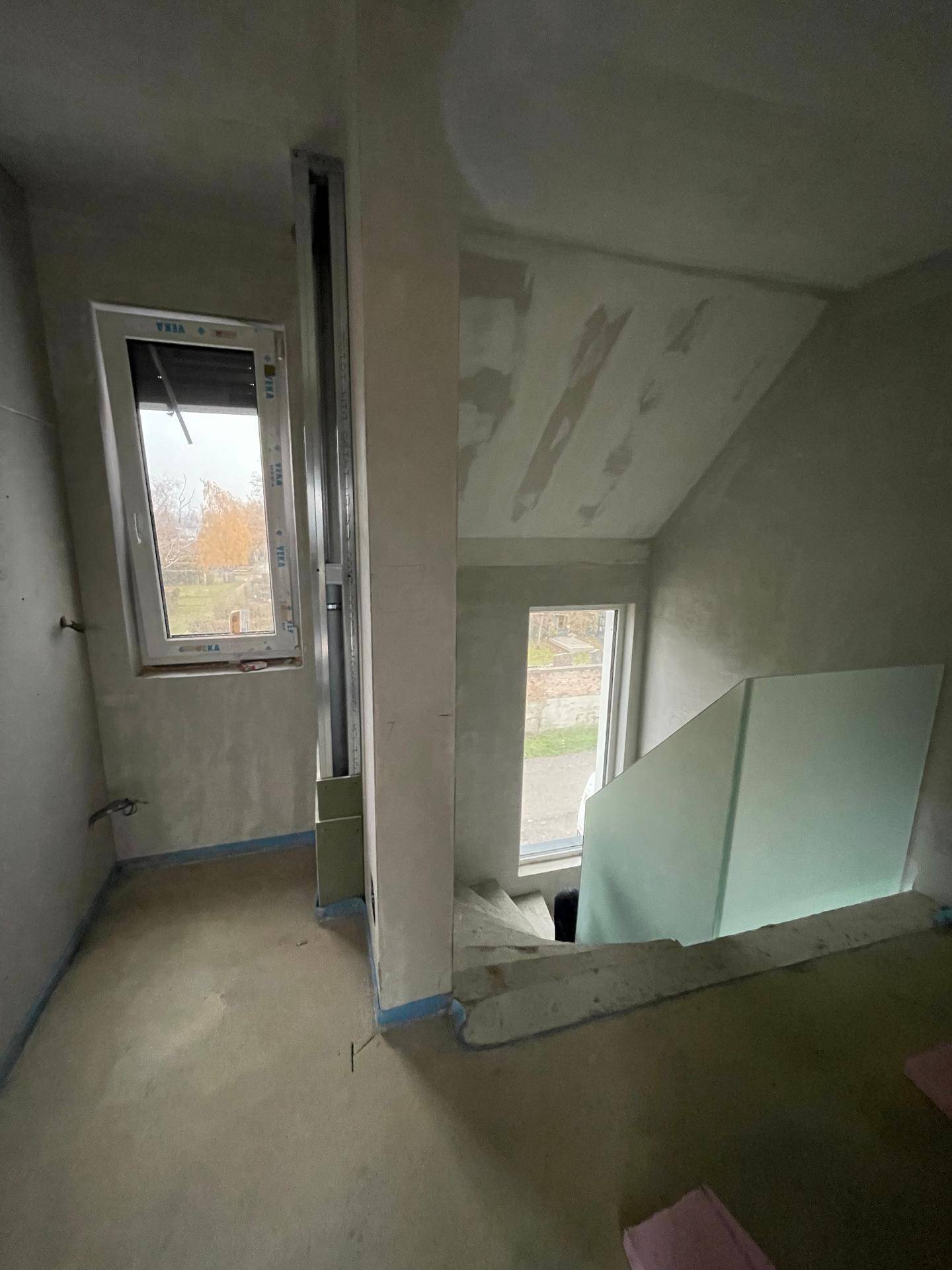 Unfertiger Flur mit Treppenaufgang und Fenster, bereit für den weiteren Ausbau.