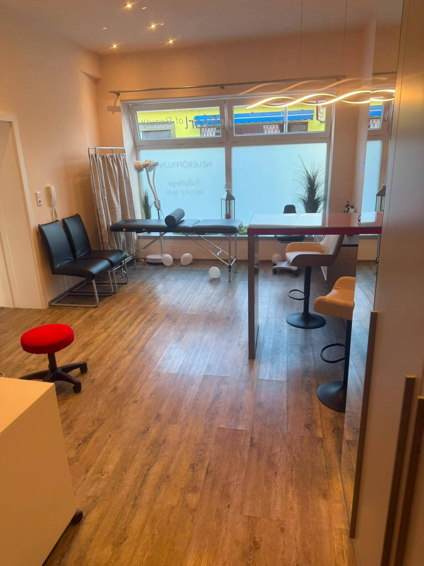 Gewerbefläche mit Massageliege, Barhockern und Laminatboden, ideal für Dienstleistungen.