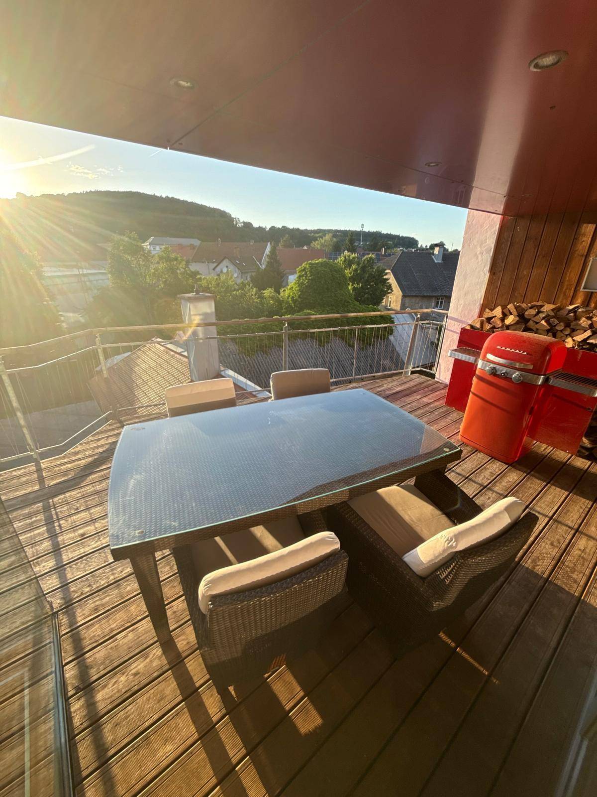 Gemütlicher Balkon mit Esstisch, Grill und weitem Blick über die Stadt bei Sonnenuntergang.