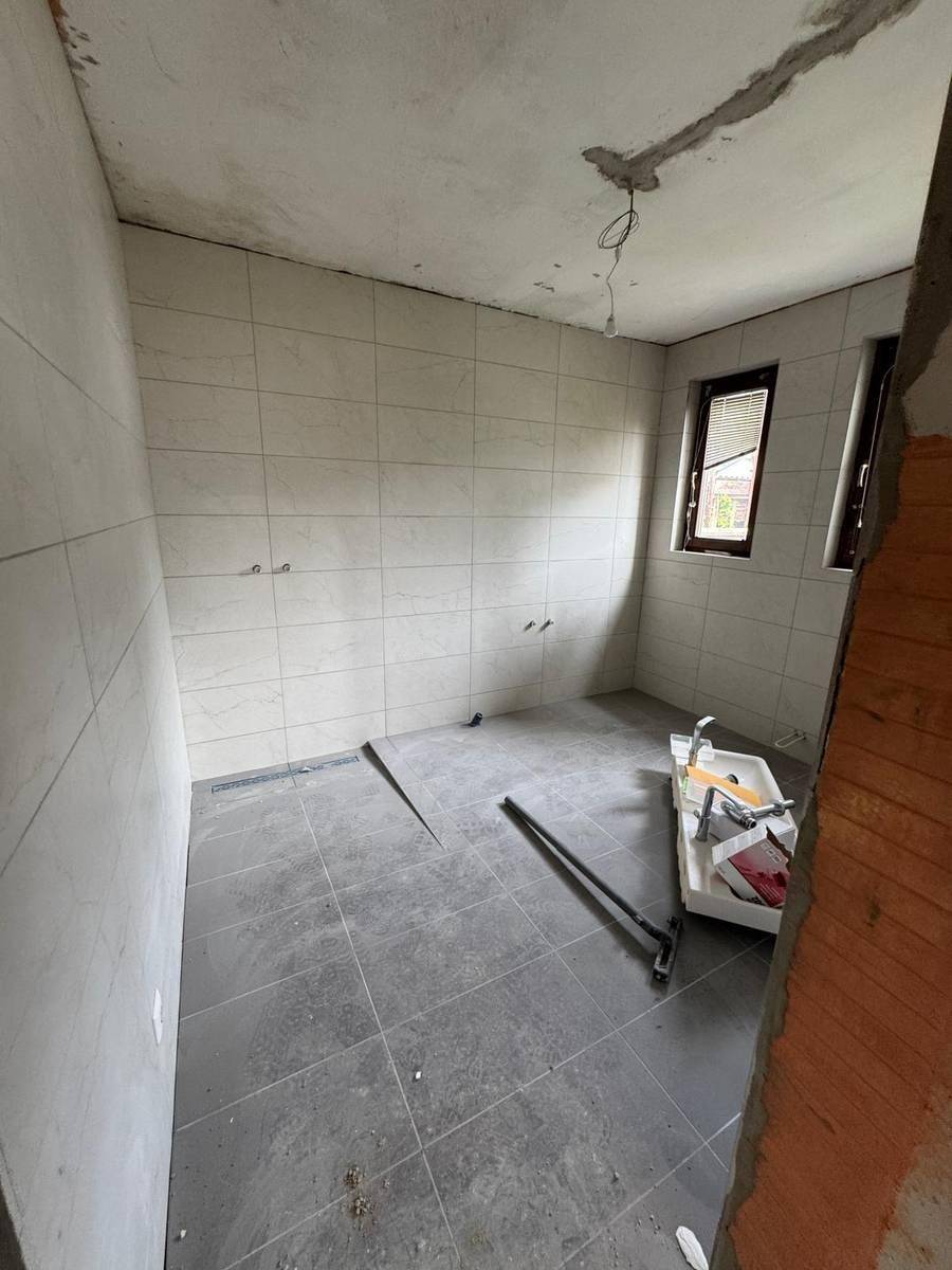Badezimmer im Rohbau mit hellen Wandfliesen und dunklem Boden, bereit für die Installation der Sanitärobjekte.