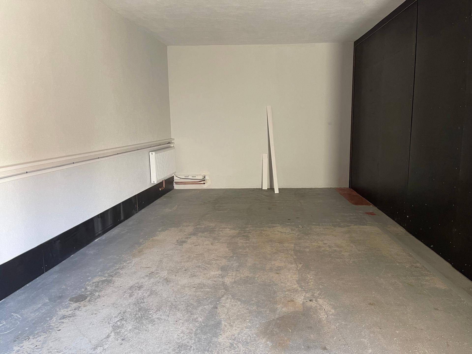 Geräumiger Garageninnenraum mit Betonboden, weißen Wänden und dunkler Seitenwand, ideal für Fahrzeuge.