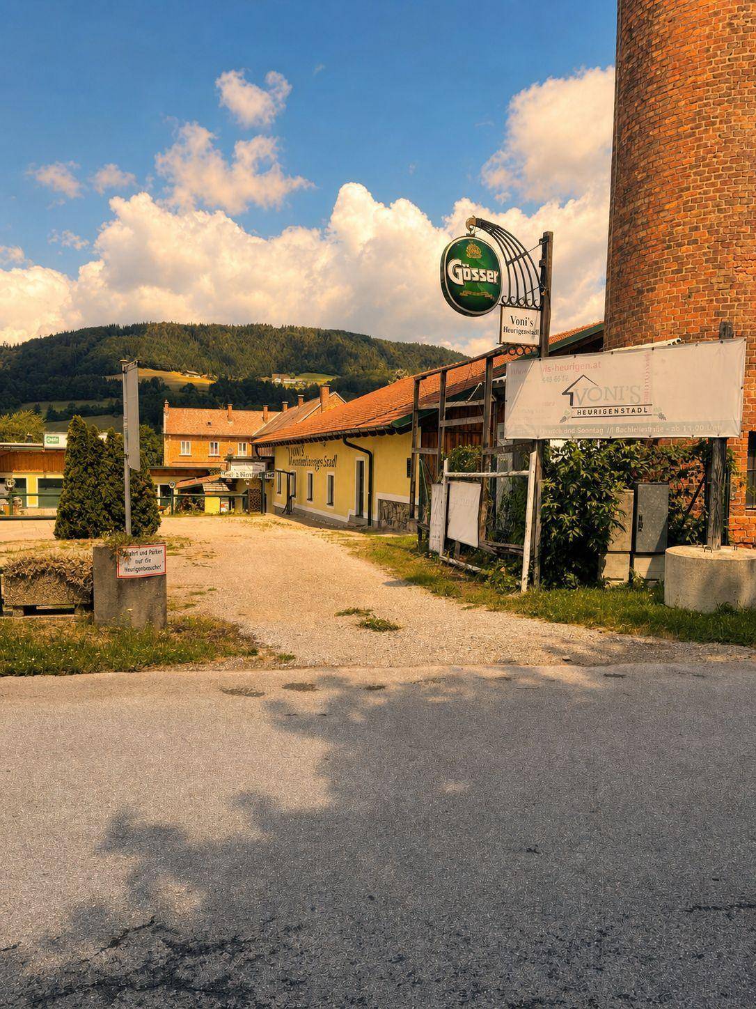 Blick auf den Gebäudekomplex von der Straße, mit Werbeschildern und dem Turm im Hintergrund.