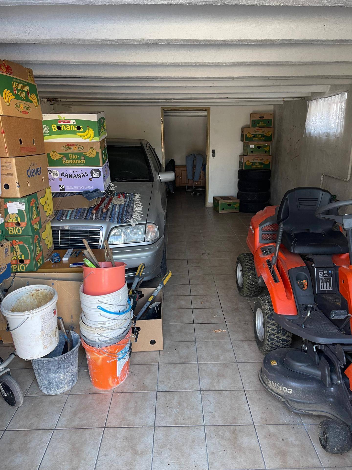 Geräumige Garage im Kellergeschoss mit Fahrzeug und Gartengeräten.