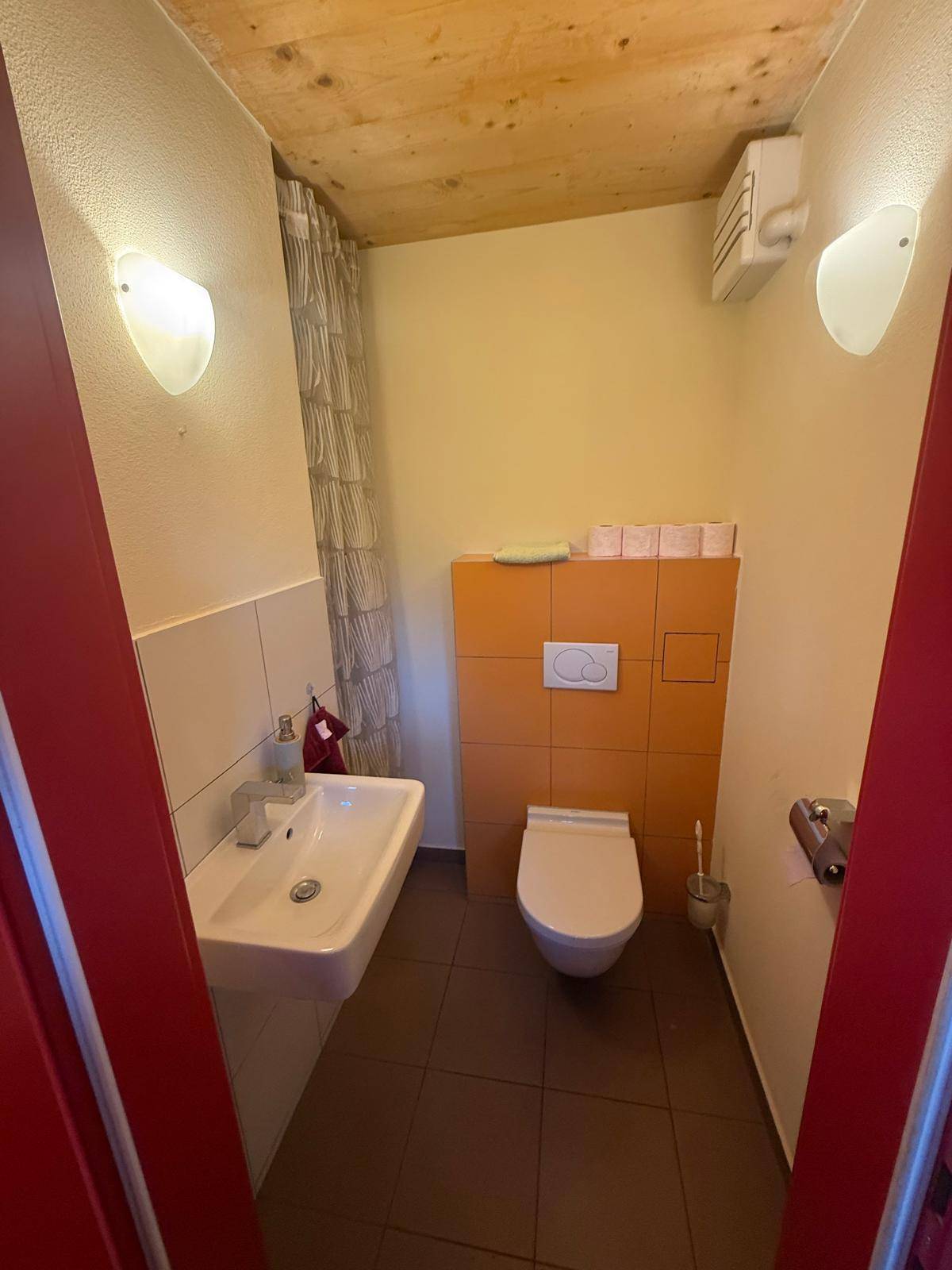 Kleines Gäste-WC mit Waschbecken, wandhängendem WC und Holzdecke.