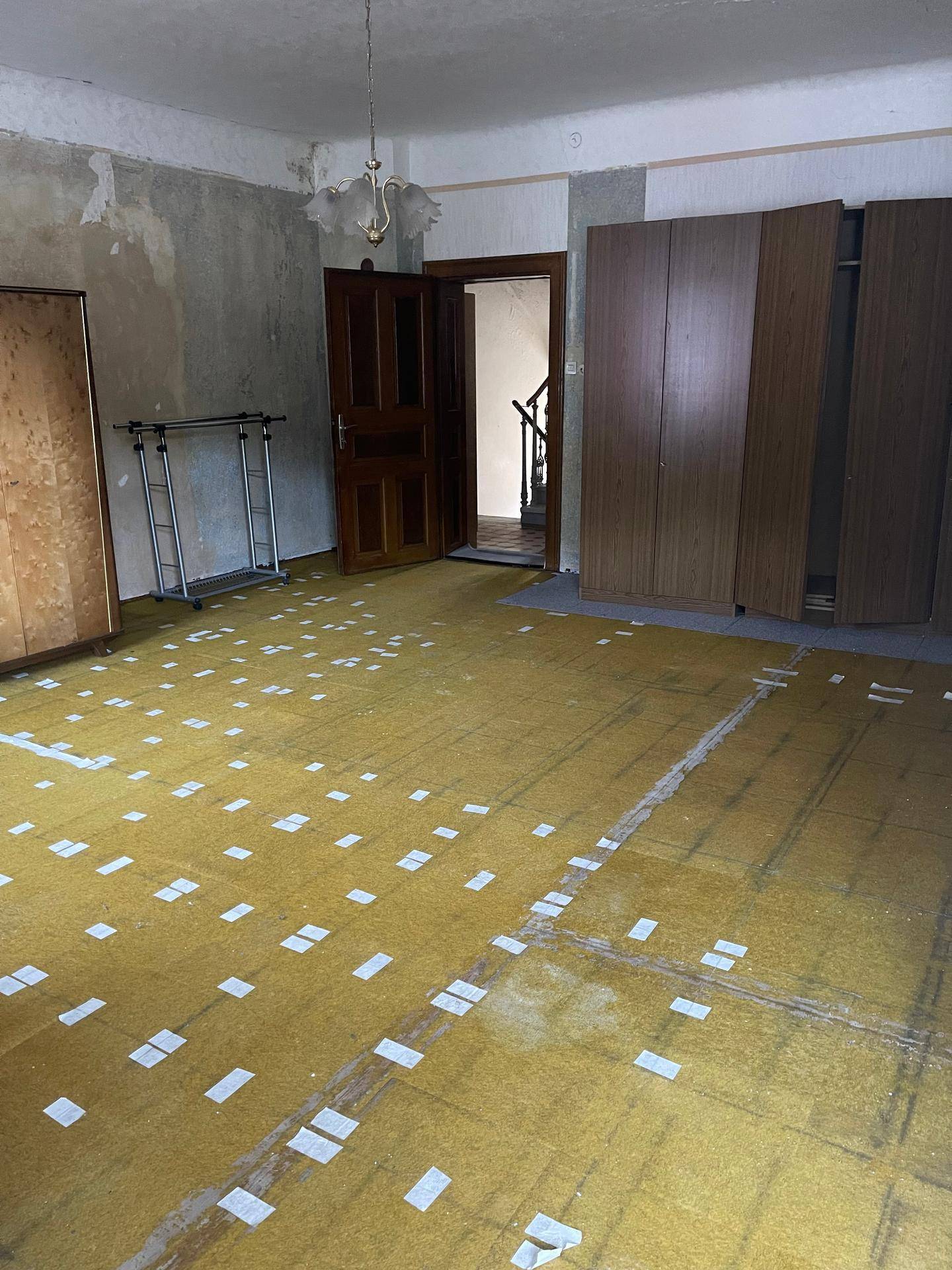 Zimmer mit gelbem Unterboden, alten Schränken und einem Fenster, das auf eine Renovierung wartet.