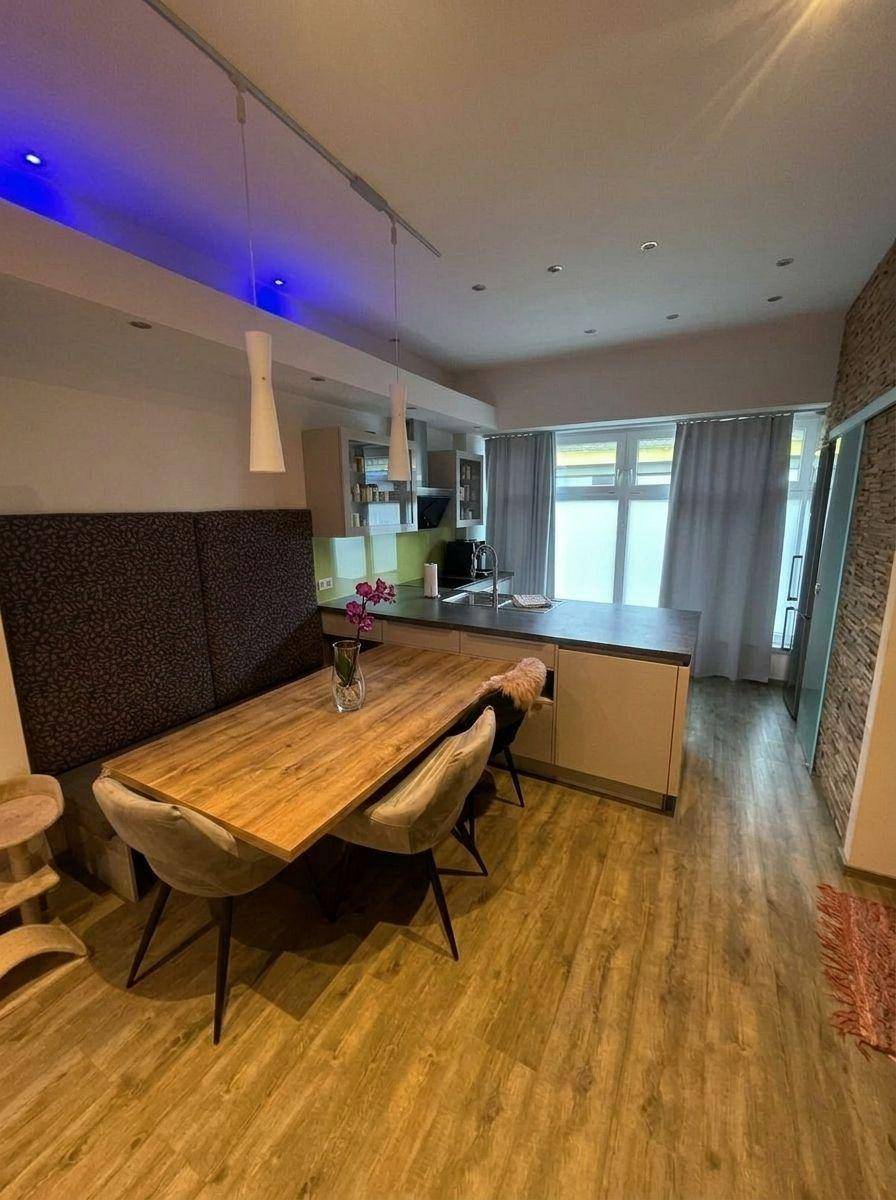 Moderne offene Küche mit Essbereich, Holzboden und stilvoller blauer Akzentbeleuchtung.