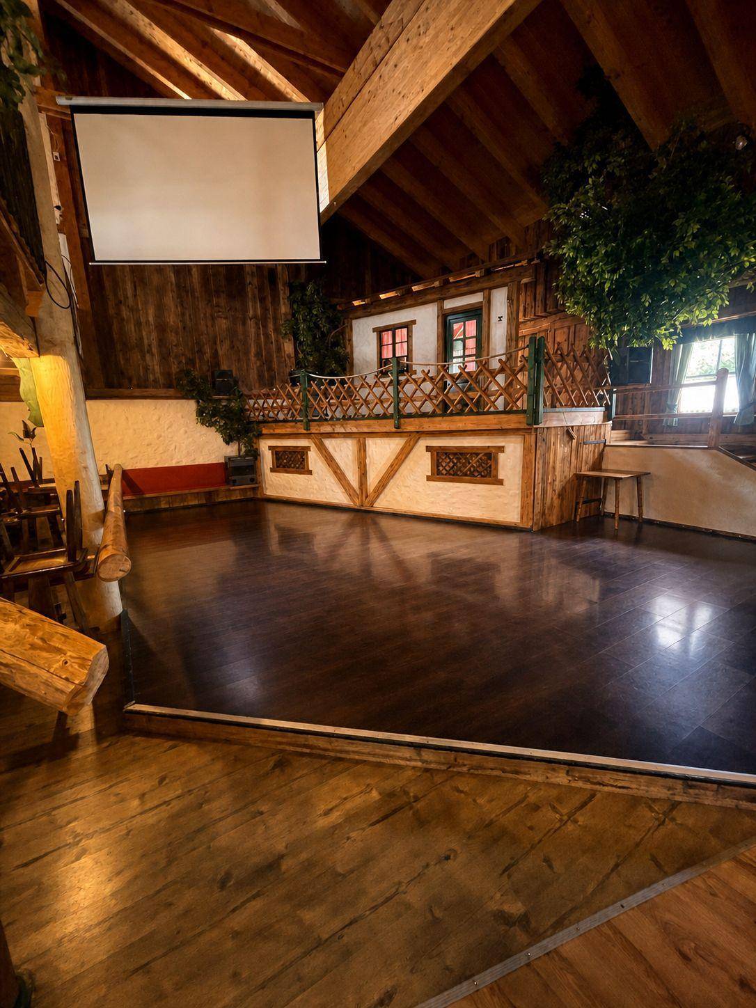 Bühne und Projektionsfläche in einem großen Saal mit Holzboden und rustikalen Holzelementen, bereit für Präsentationen.