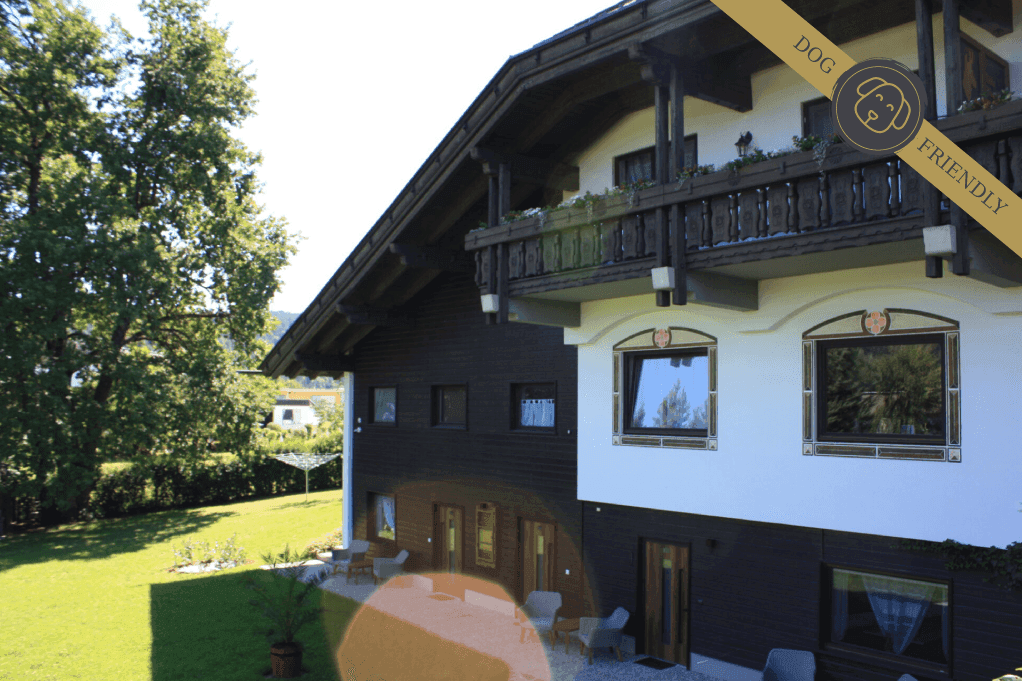 Traditionelles Gebäude mit Holzbalkonen und gepflegtem Garten, umgeben von viel Grün.