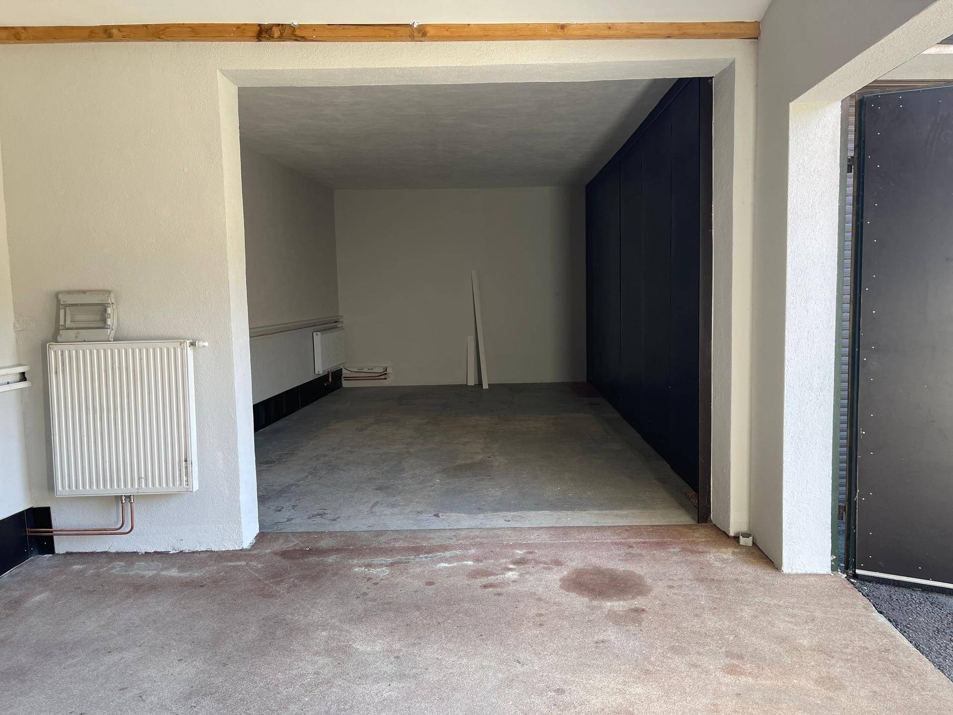 Tiefer Garagenraum mit Betonboden, weißen Wänden und einer dunklen Seitenwand, die auf Lagerung hindeutet.