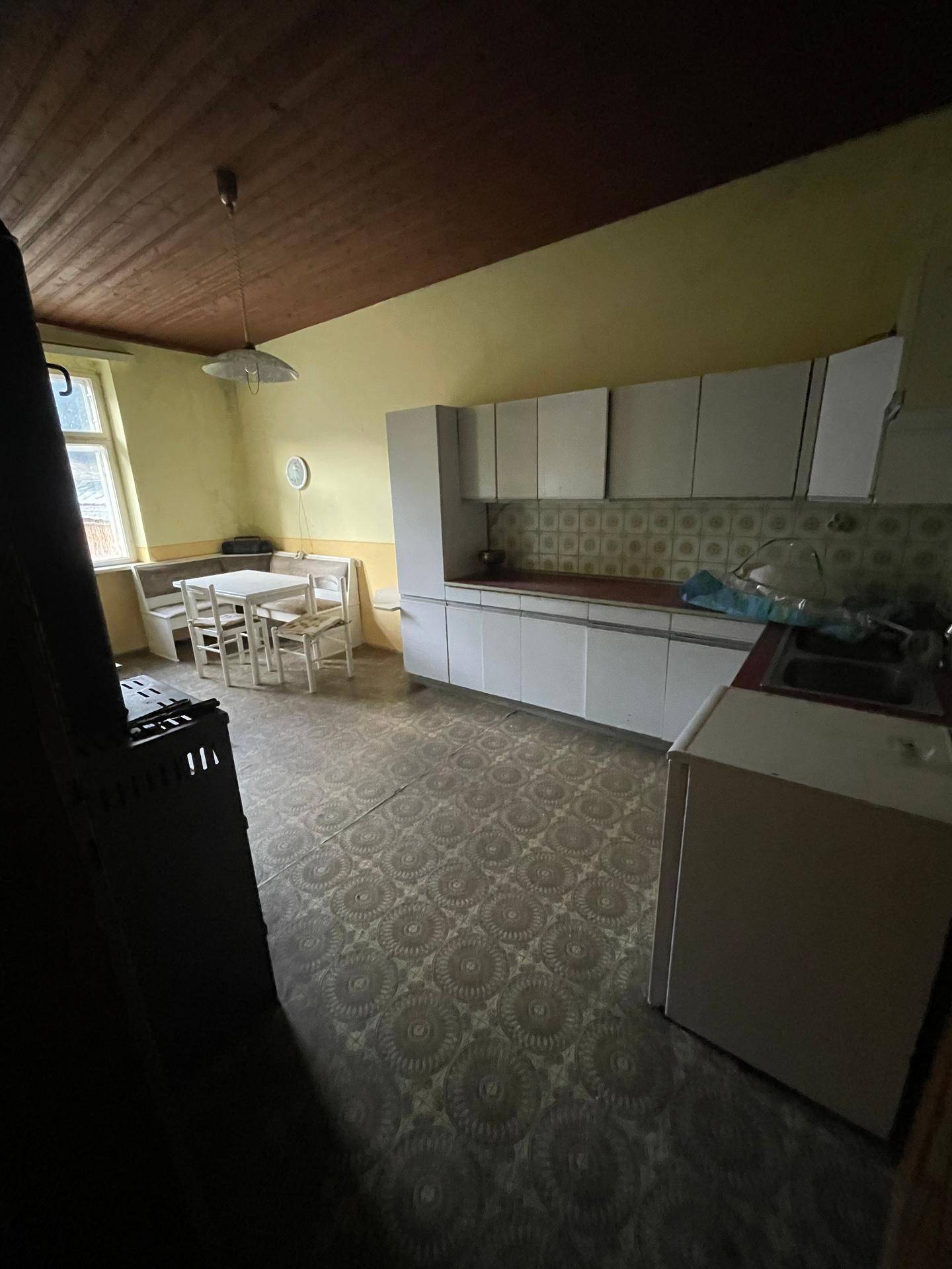 Rustikale Küche mit alten Einbauschränken, Holzofen und Essbereich, der Renovierung bedarf.
