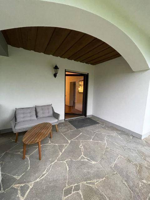 Überdachte Terrasse mit Steinboden und Sitzgelegenheit, bietet einen geschützten Außenbereich.