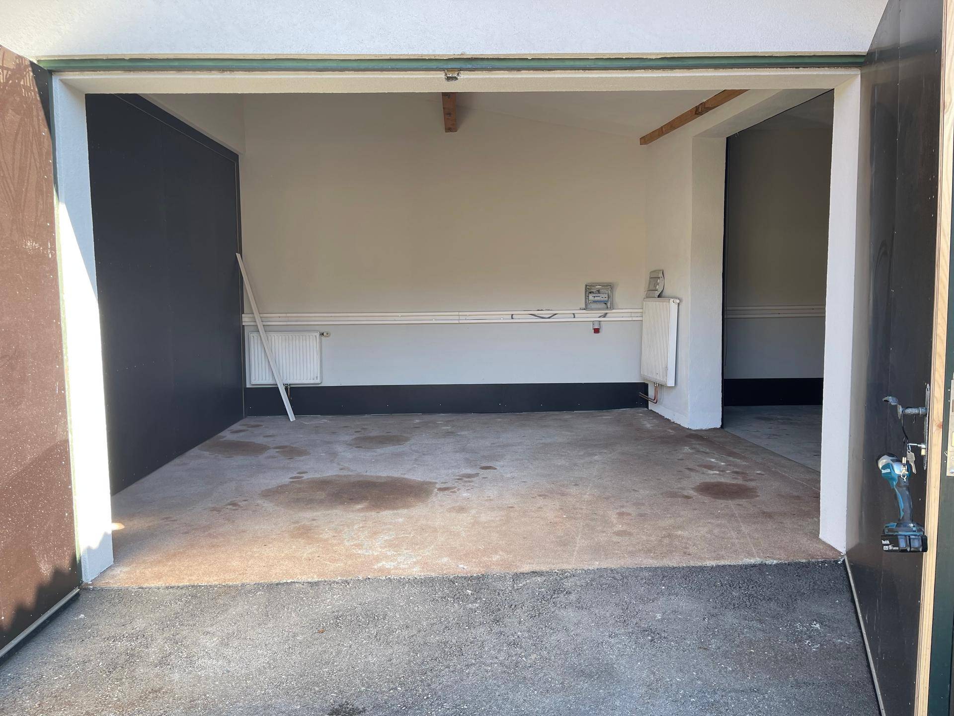 Geräumiger Garageninnenraum mit Betonboden, Heizkörpern und sichtbaren Holzbalken, bereit zur Renovierung.