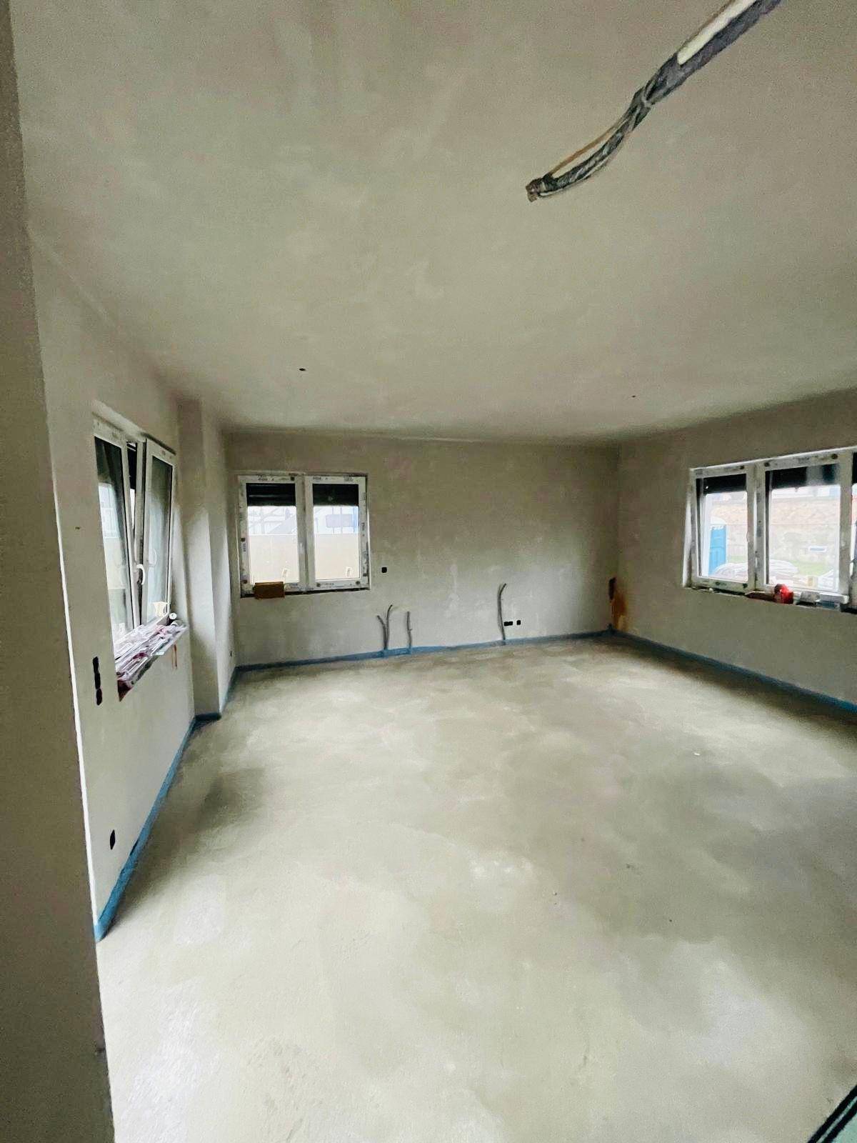 Großer Rohbau-Raum mit Estrichboden und vielen Fenstern, ideal für individuelle Gestaltung.