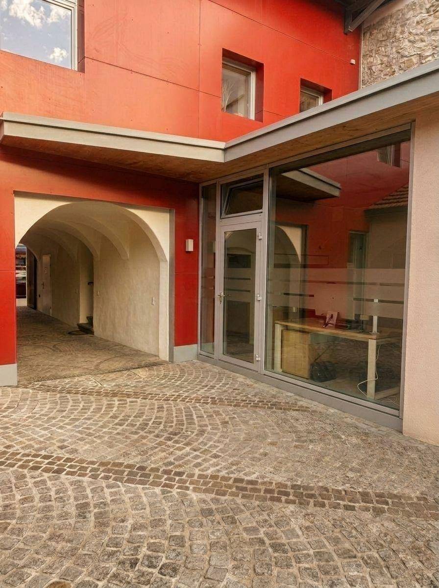 Nahaufnahme des modernen Gebäudeeingangs mit Glasfassade und gepflastertem Innenhof.