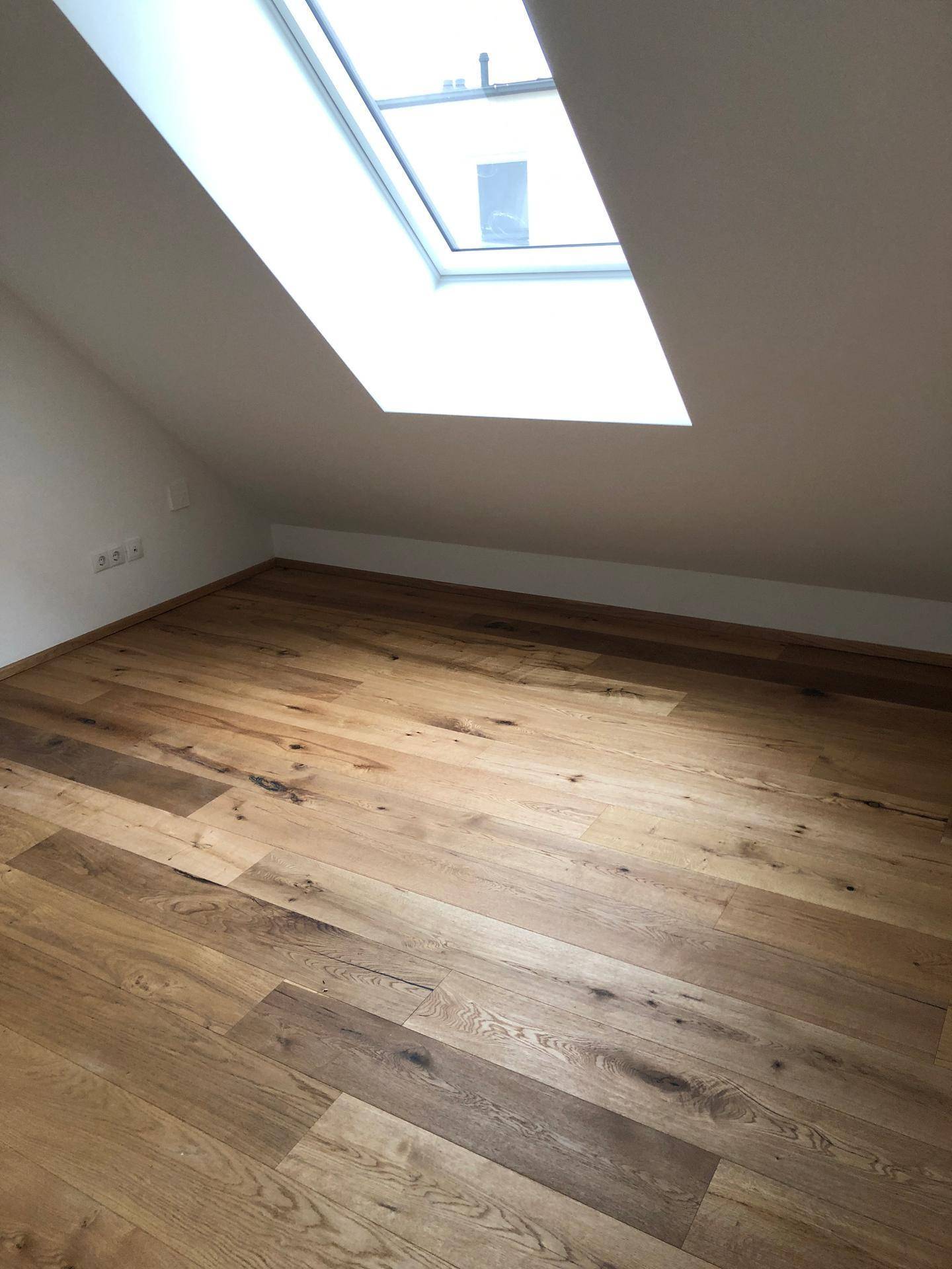 Dachgeschosszimmer mit hellem Holzboden und einem großen Dachfenster für viel Tageslicht.