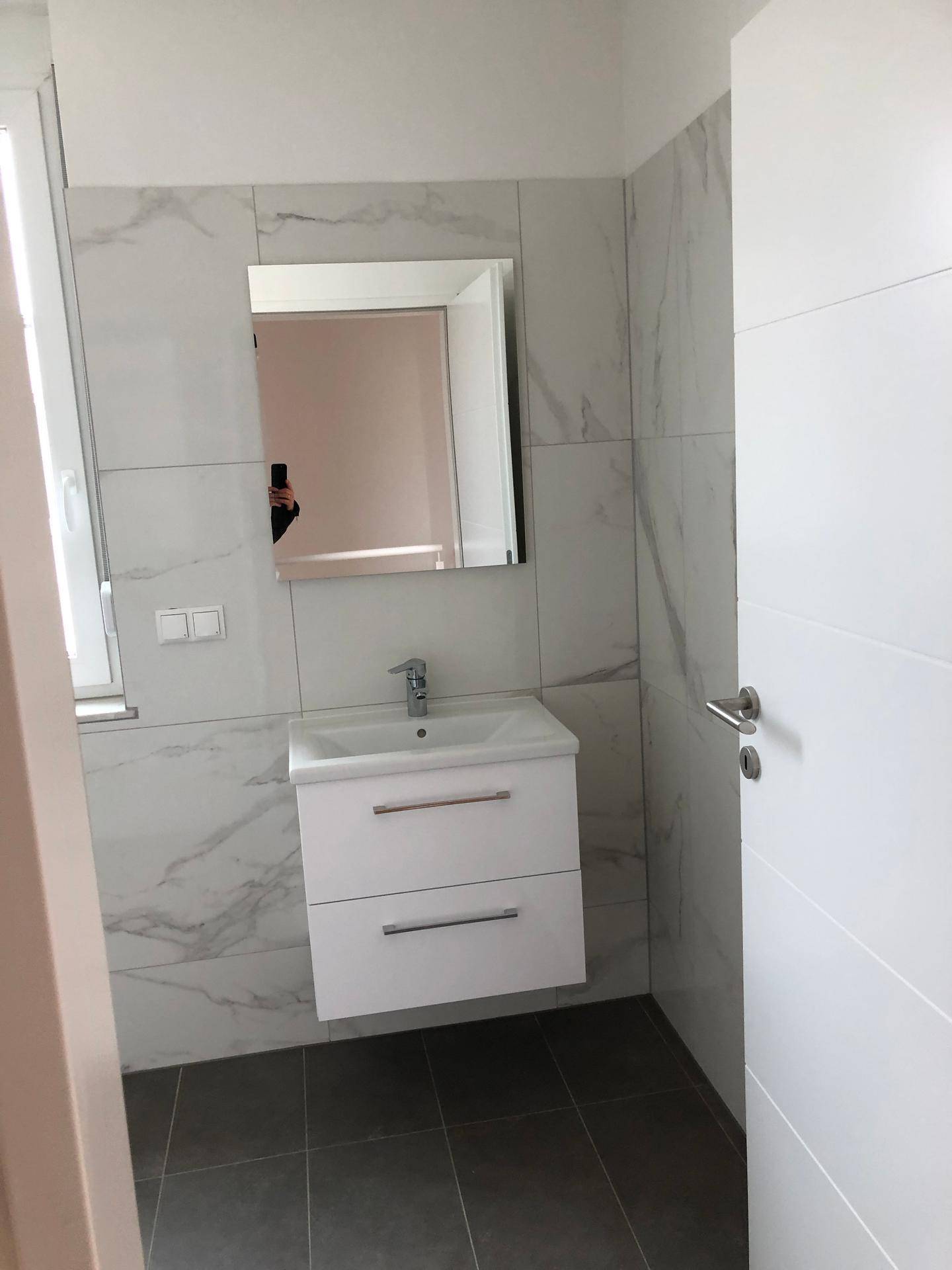 Modernes Badezimmer mit weißem Waschtisch, Spiegel und großformatigen Marmorfliesen.