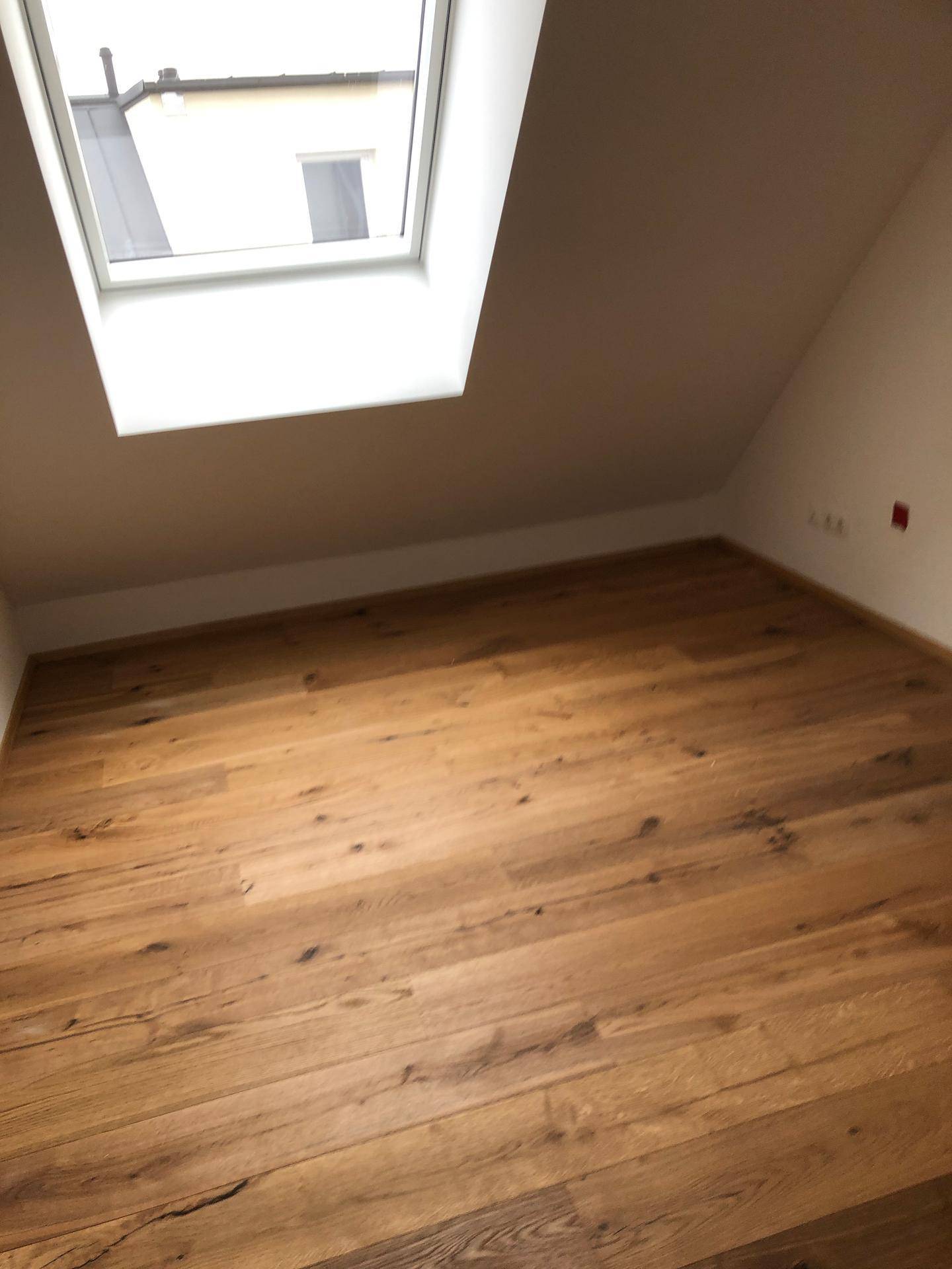 Dachgeschosszimmer mit Holzboden und einem großen Dachfenster, das den Raum erhellt.