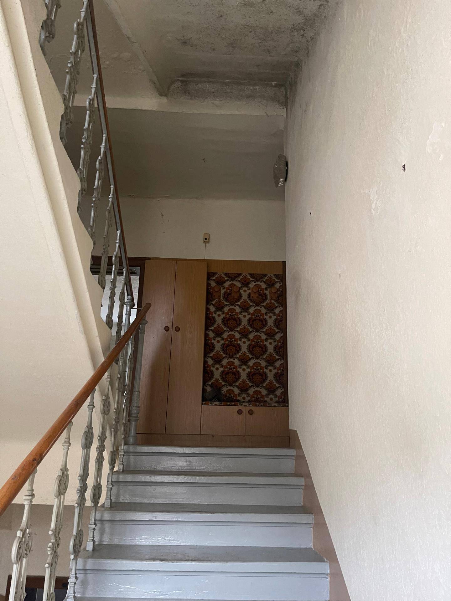 Treppenaufgang mit schmiedeeisernem Geländer und einem Schrank mit gemusterter Tapete im Hintergrund.