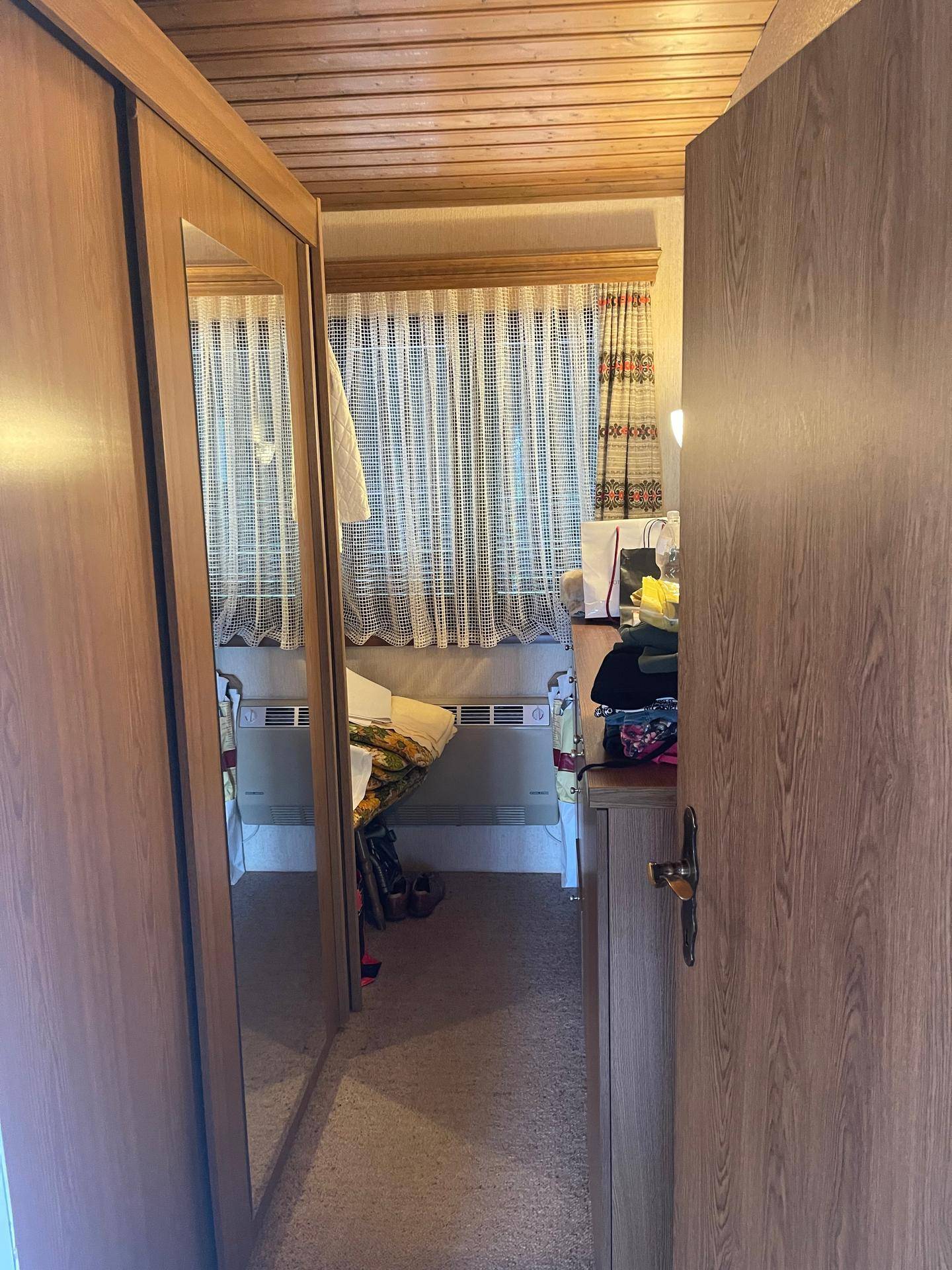 Schlafzimmer mit Holzschränken und einem Fenster mit Vorhängen, das Tageslicht hereinlässt.
