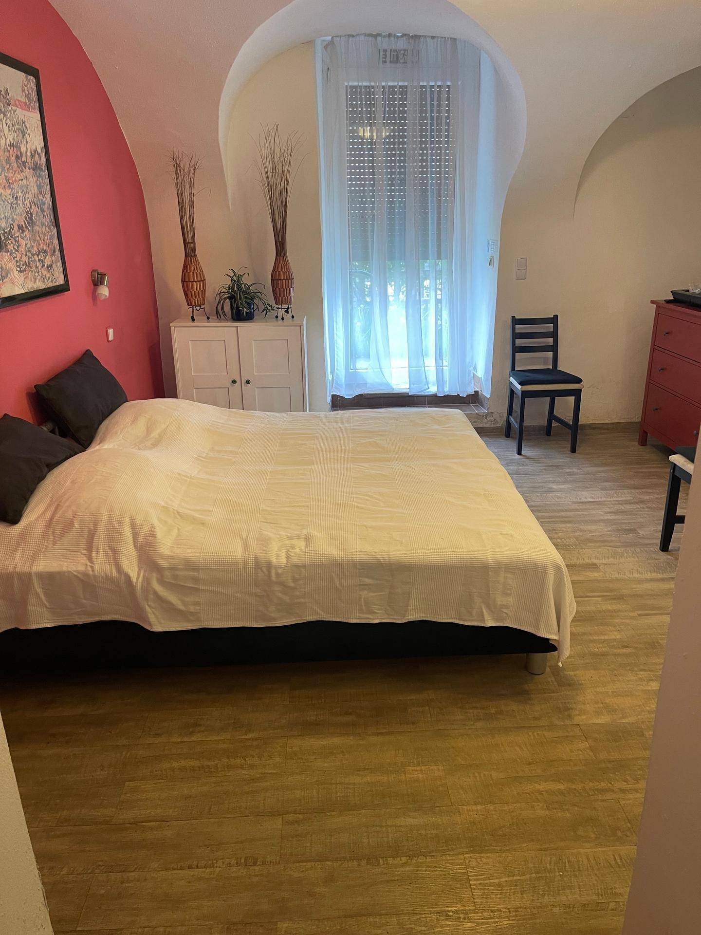 Schlafzimmer mit gewölbter Decke, roter Akzentwand und Holzboden.
