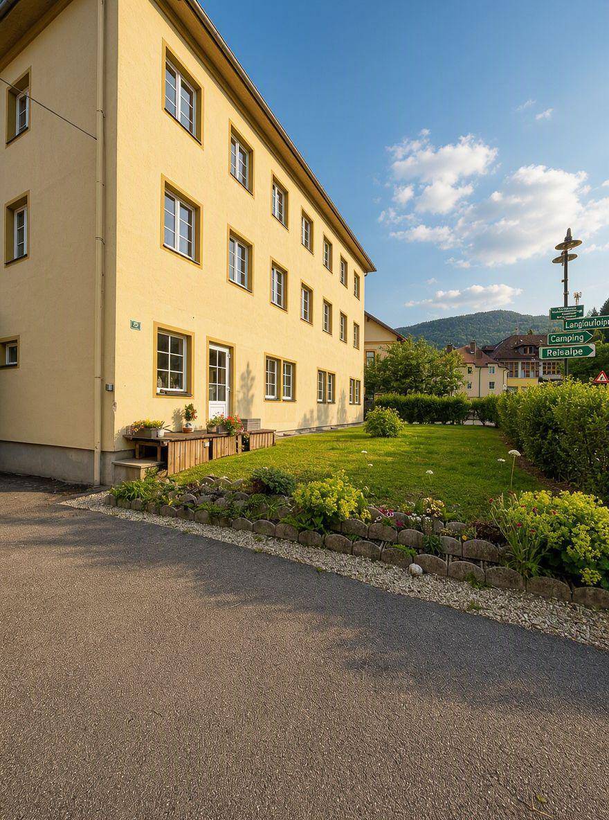 Seitenansicht des gelben Gebäudes mit gepflegtem Rasen und Blumenbeeten im Vorgarten.
