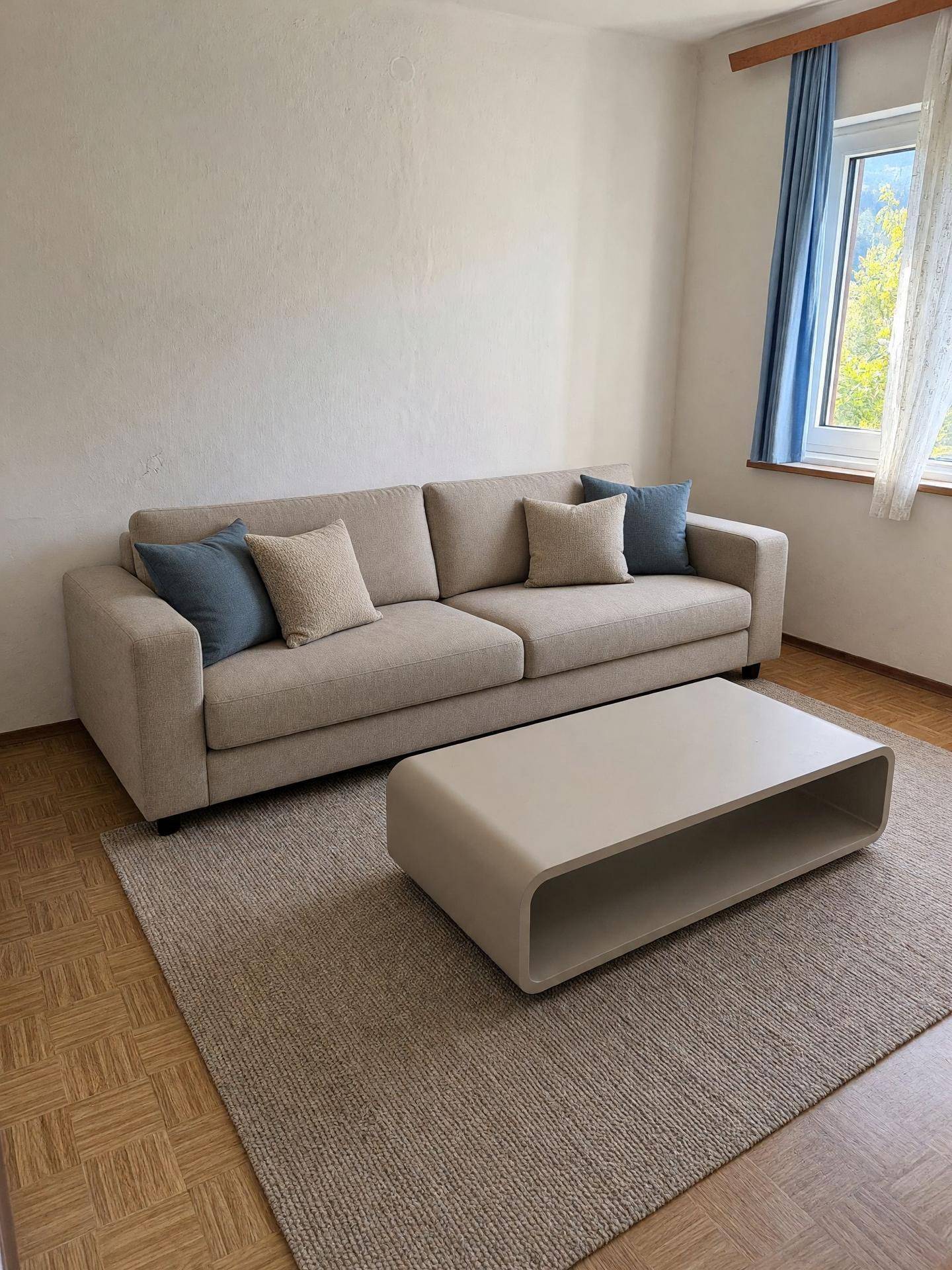 Modernes Wohnzimmer mit beigem Sofa, Couchtisch und Parkettboden.