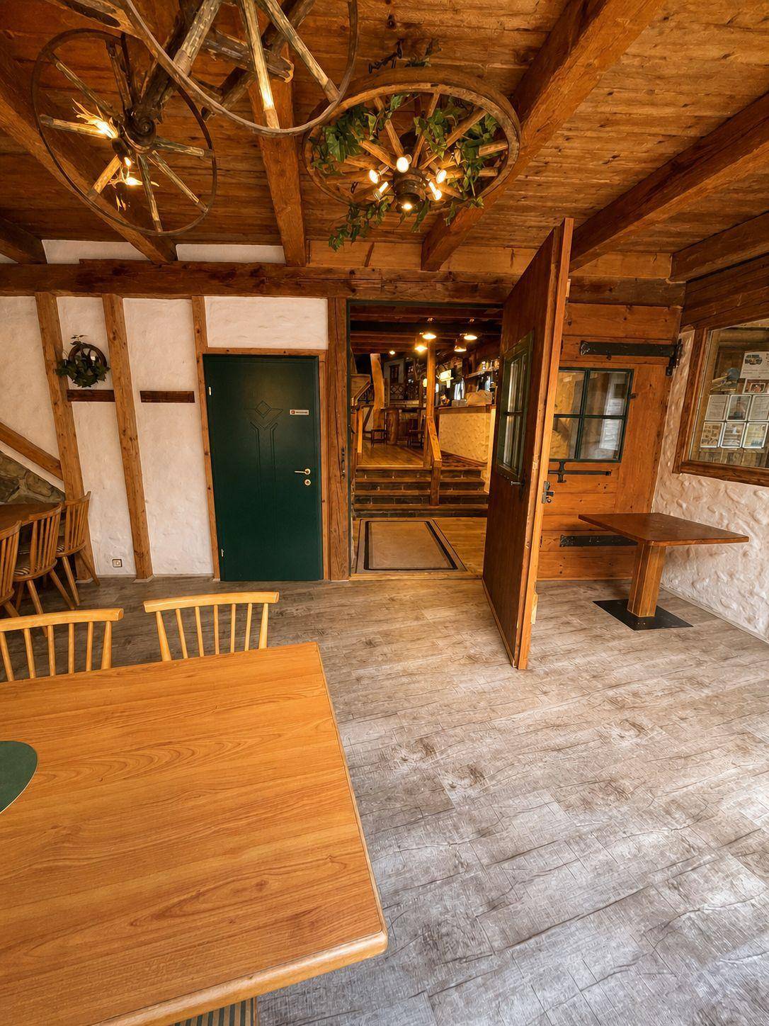 Geräumiger Essbereich mit Holztischen, Holzbalkendecke und einem Blick in einen weiteren, offen gestalteten Raum.
