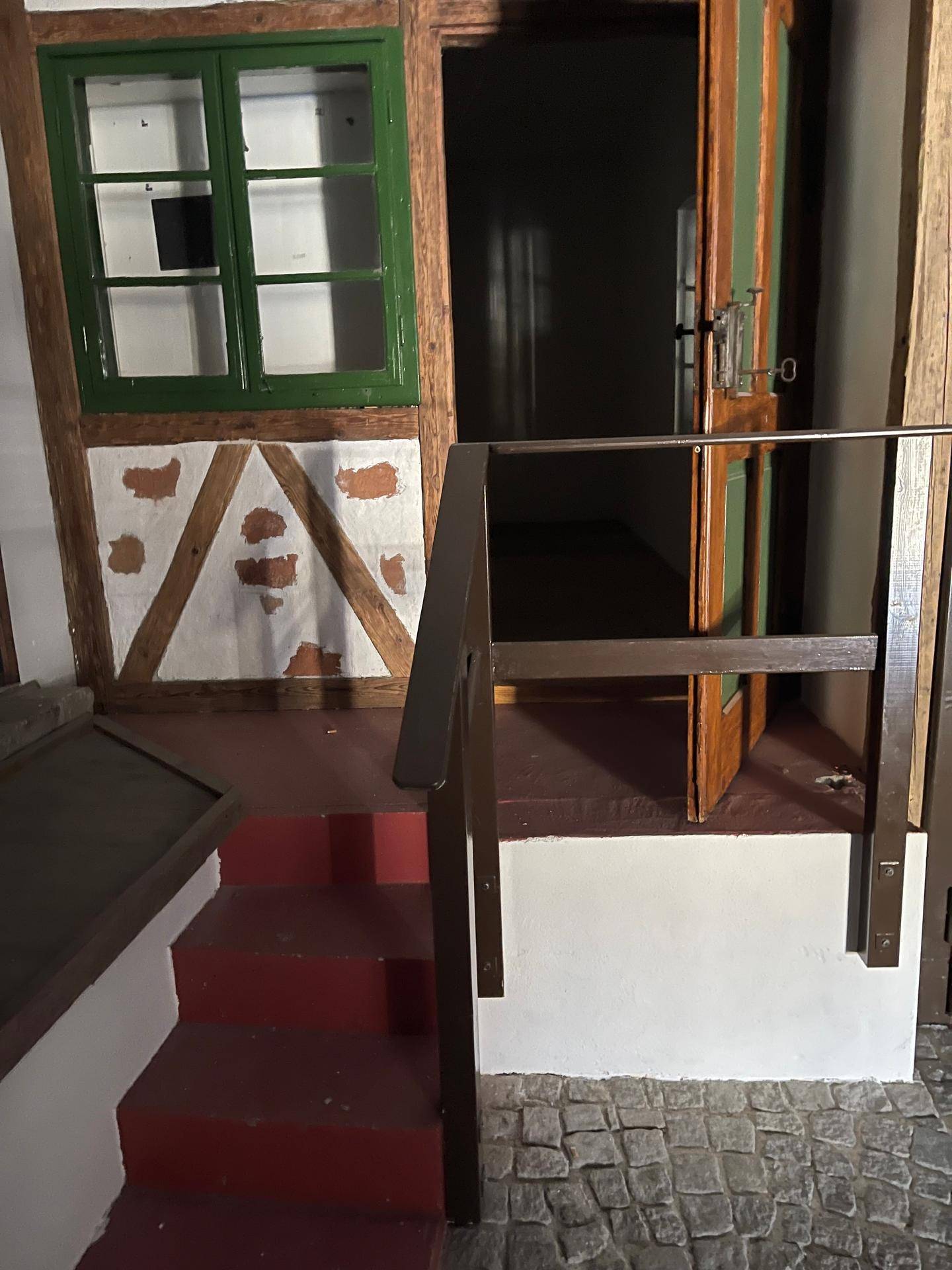 Thematischer Innenraum mit kleiner roter Treppe, grünem Fensterrahmen und rustikalen Holzelementen.