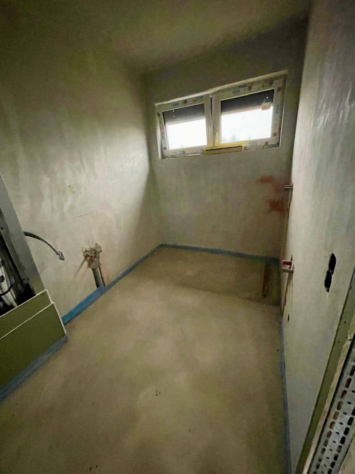 Kleiner Rohbau-Raum mit Estrichboden und Fenster, vorbereitet für Sanitärinstallationen.